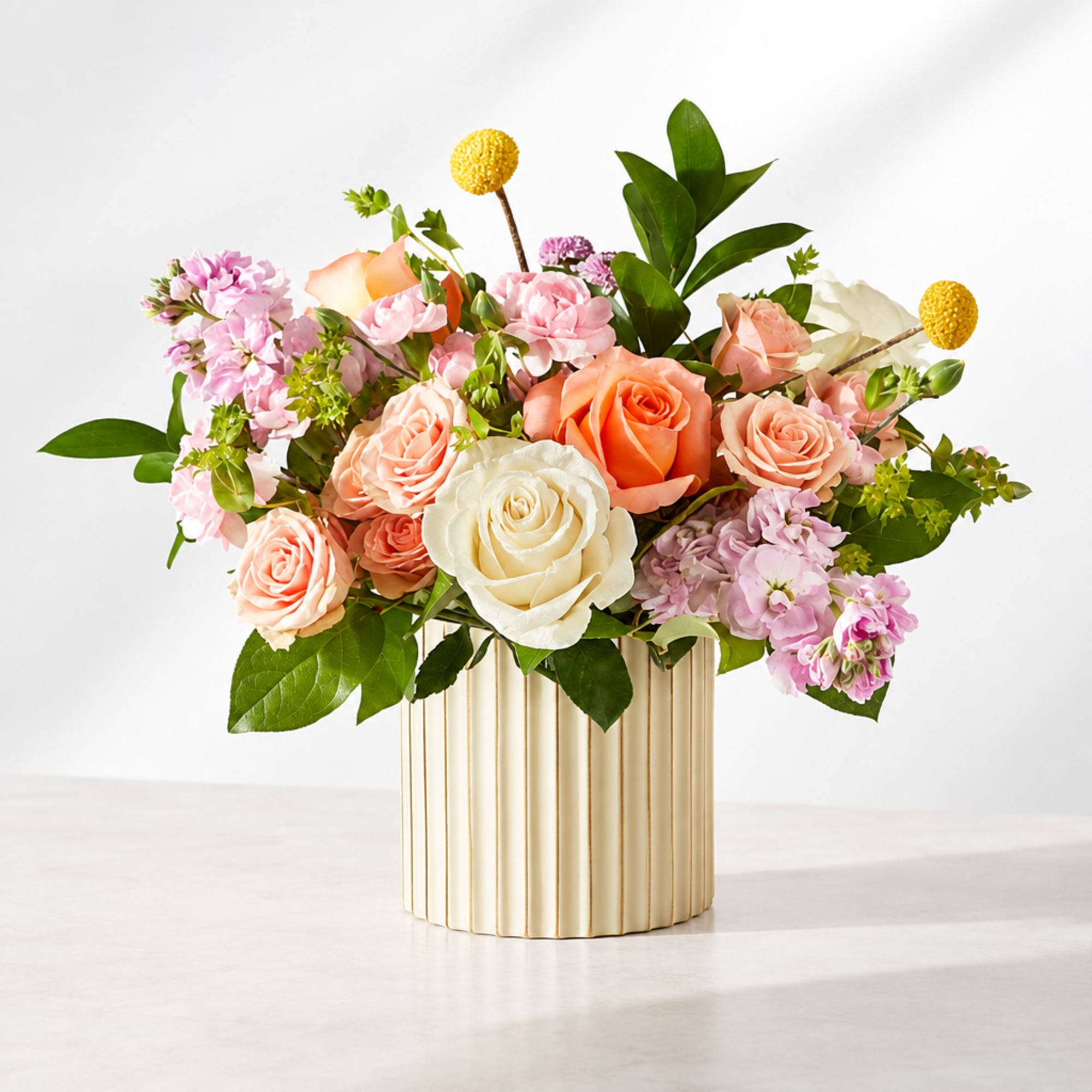 Mixed bouquet of peach, pink, and white roses in a ribbed cream vase