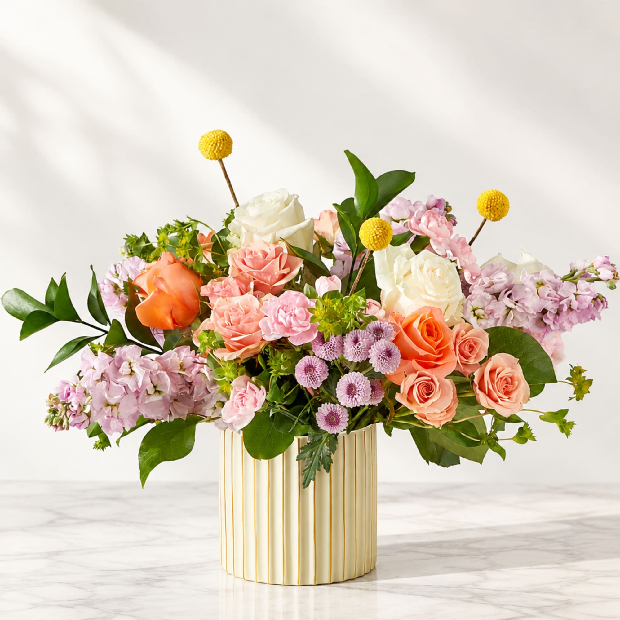 Mixed bouquet of roses and pastel flowers in a striped gold vase