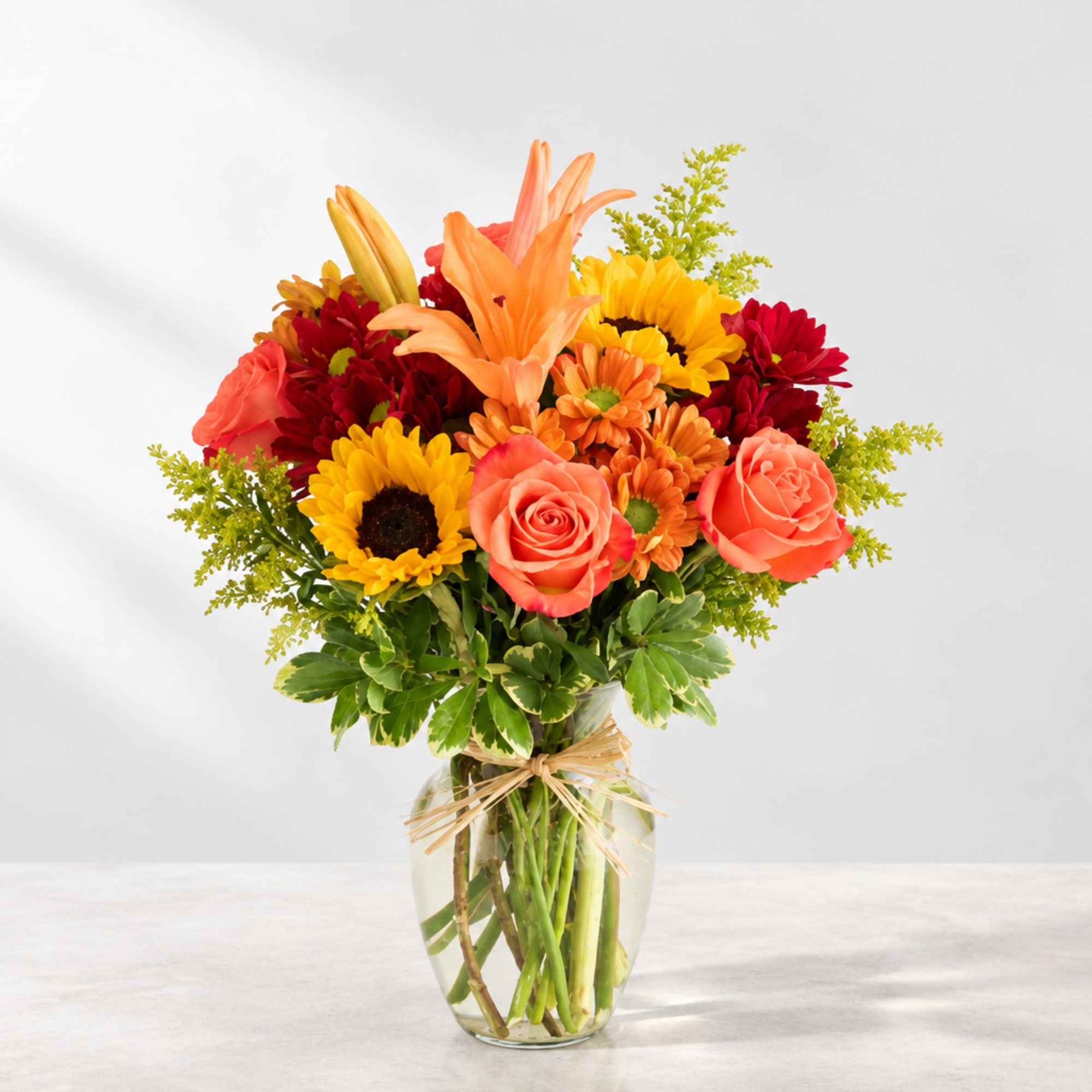 Bright mixed bouquet with roses, lilies, sunflowers, and daisies in a glass vase