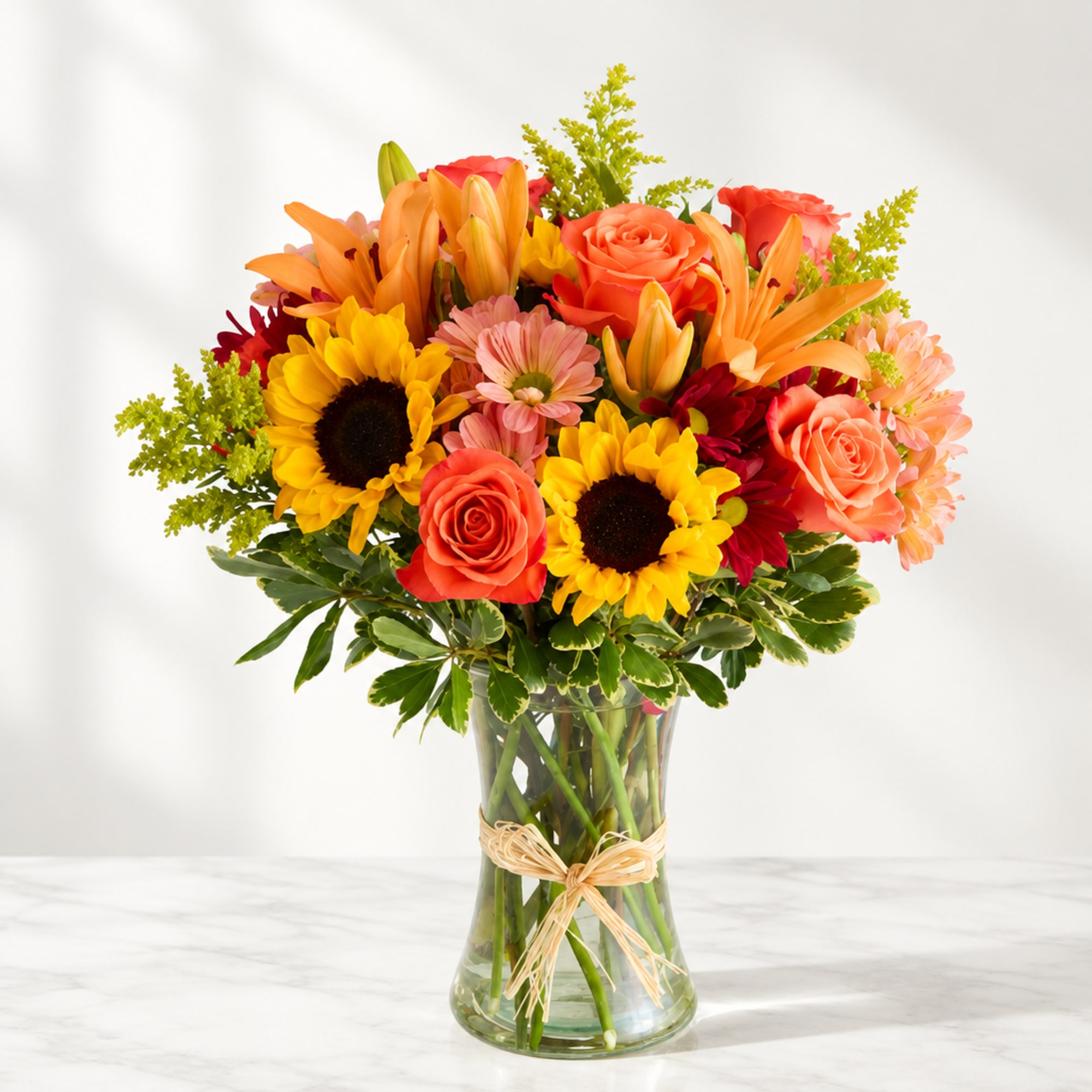 Bright mixed bouquet of roses, lilies, and sunflowers in a glass vase