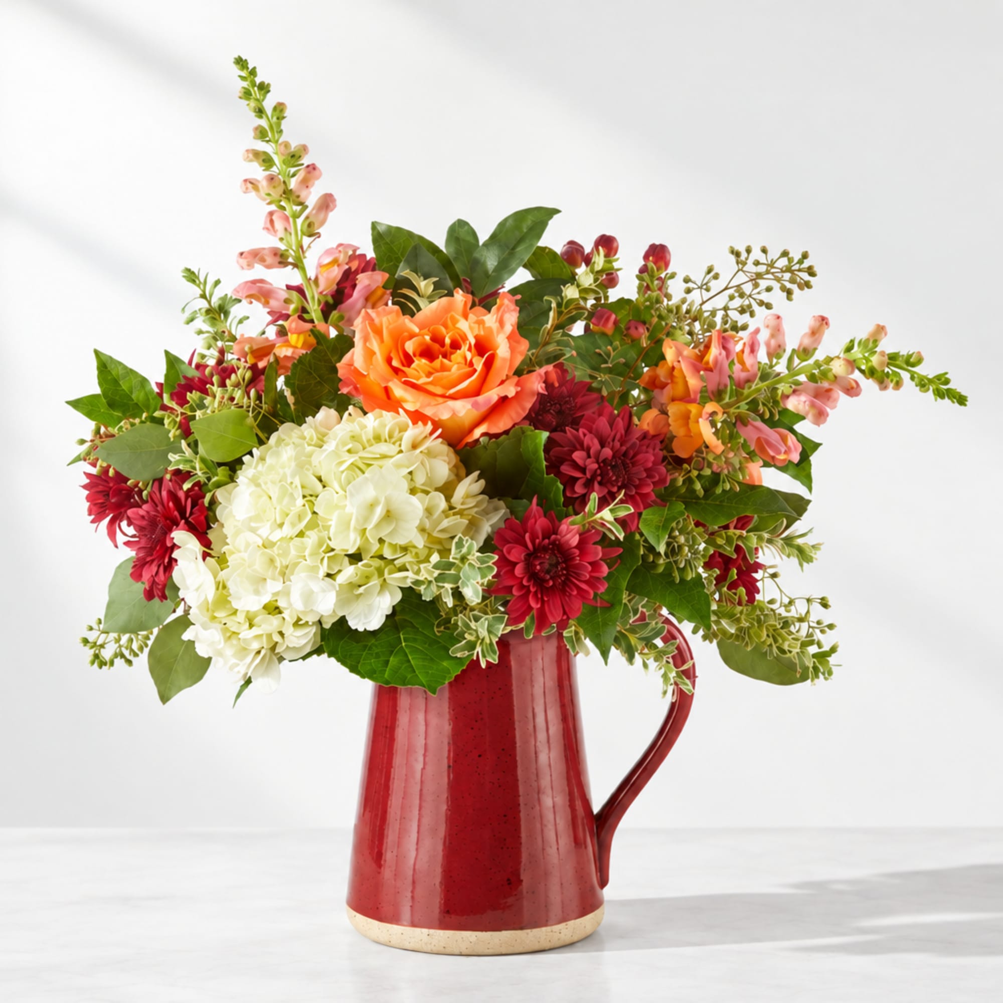 Mixed bouquet in a red ceramic pitcher with orange, white, and red blooms
