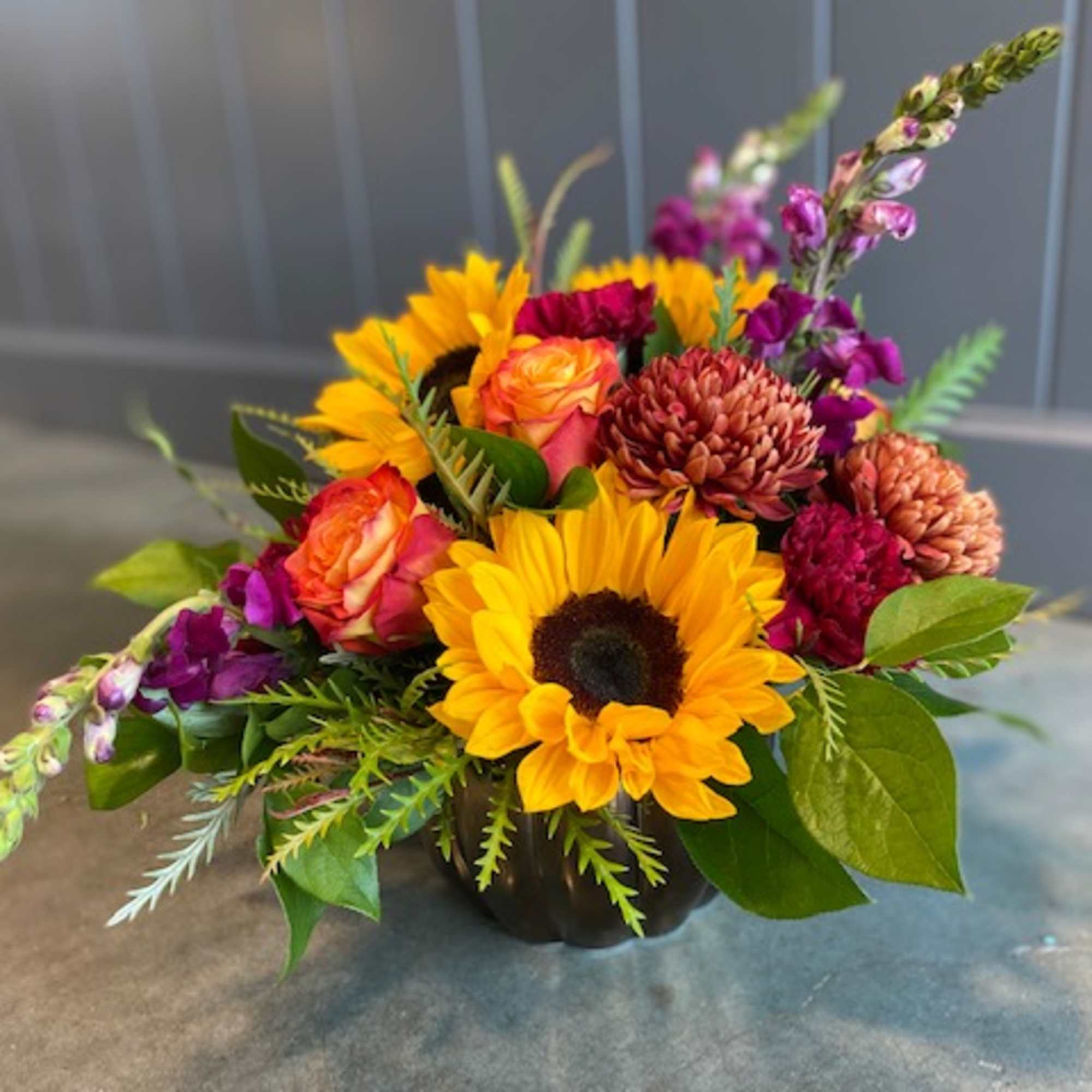 Mixed bouquet with sunflowers, roses, and purple blooms in a dark vase