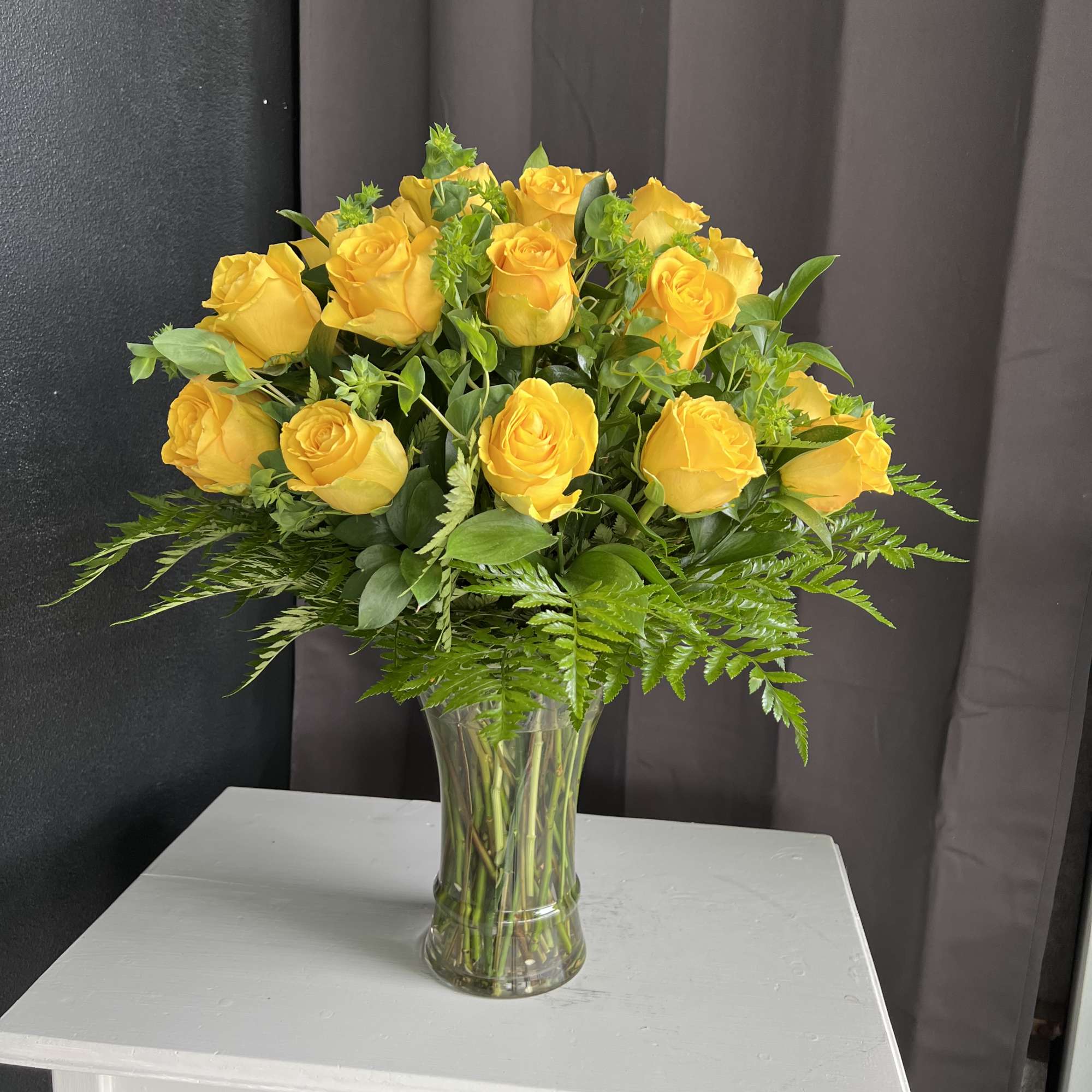 Yellow roses arranged in a clear glass vase with fern foliage