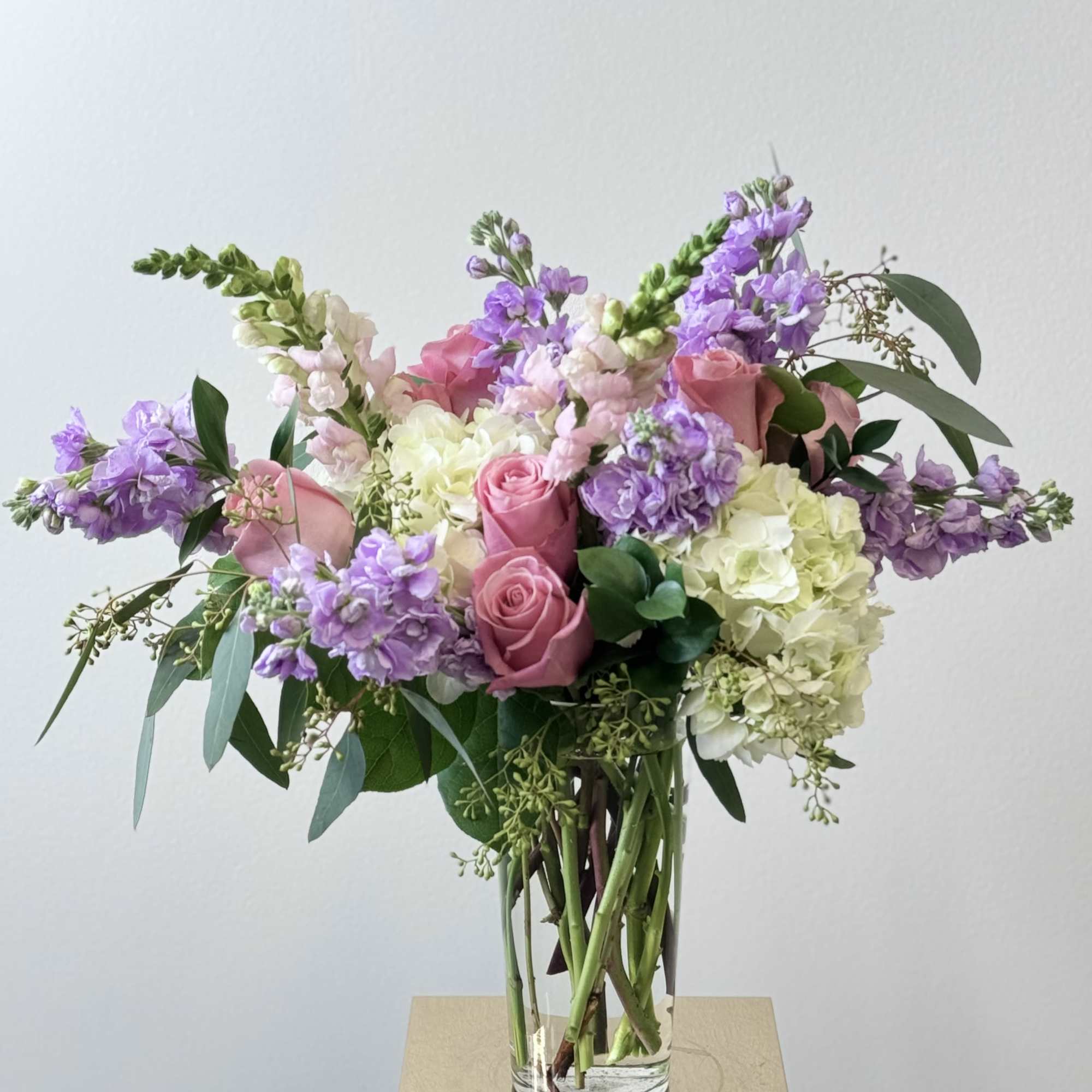 Pink roses and purple blooms in a clear glass vase