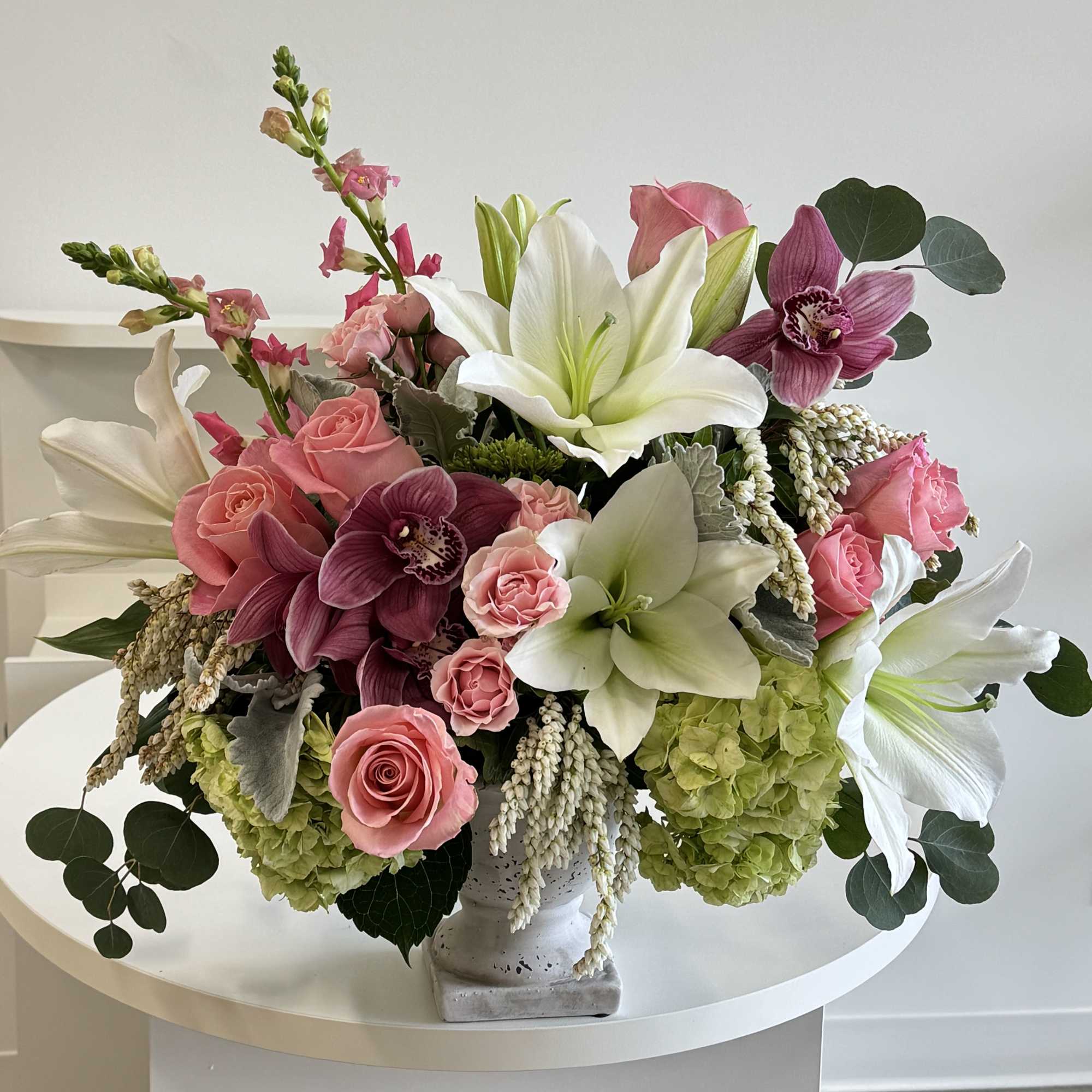 Pink roses and white lilies in a white vase with green hydrangeas