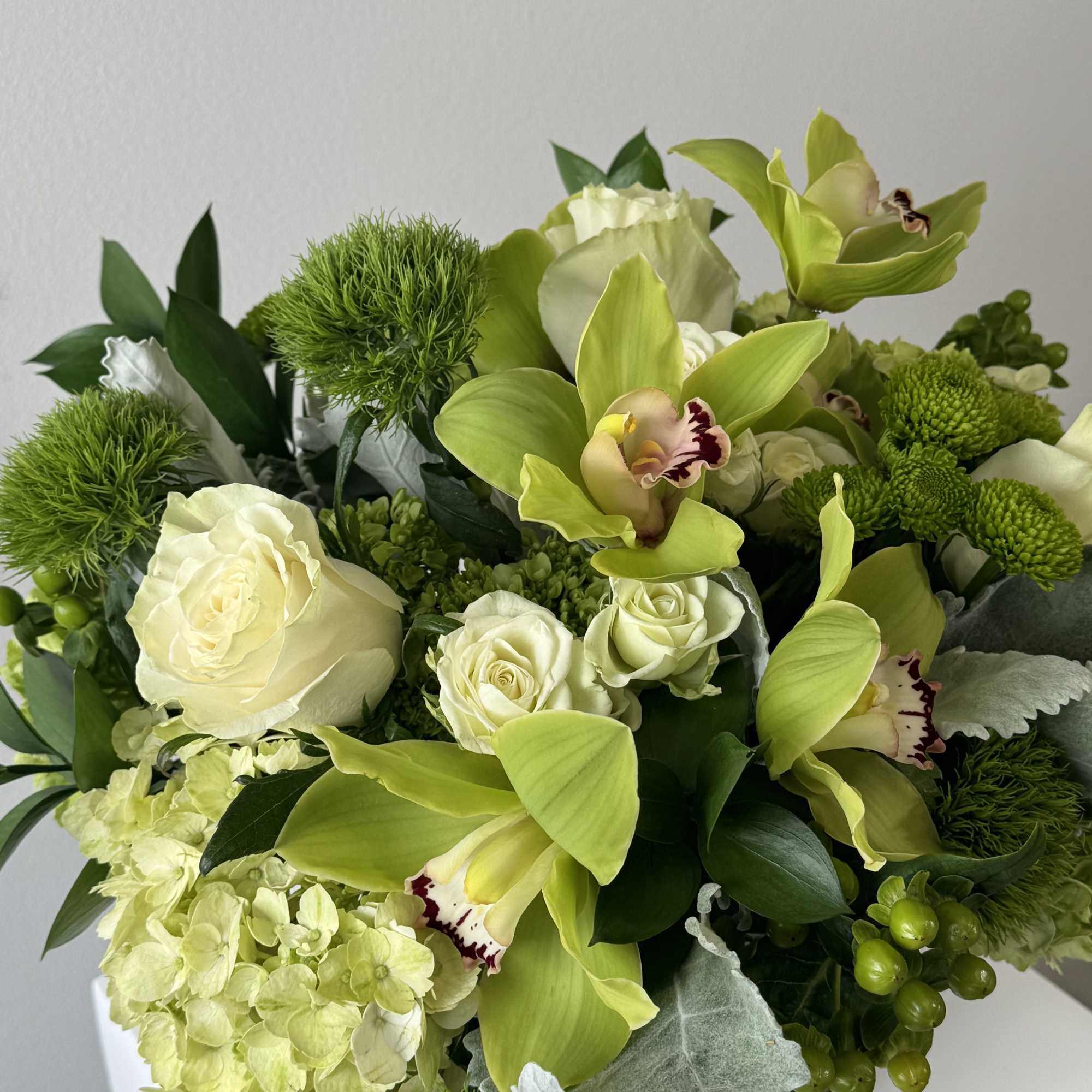 Green and white bouquet with orchids, roses, and hydrangea in a vase
