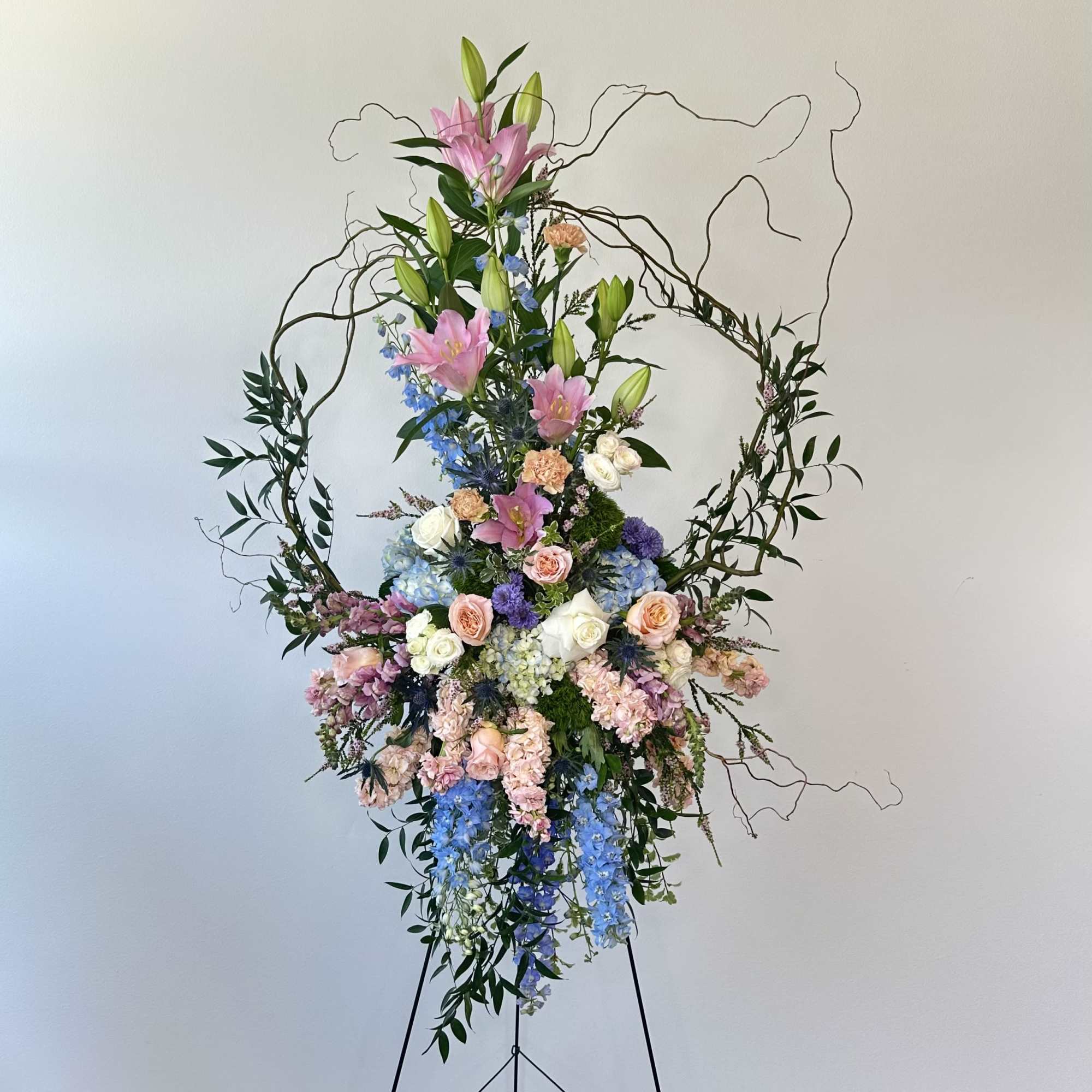 Tall floral arrangement with pink lilies, roses, and blue flowers on a stand
