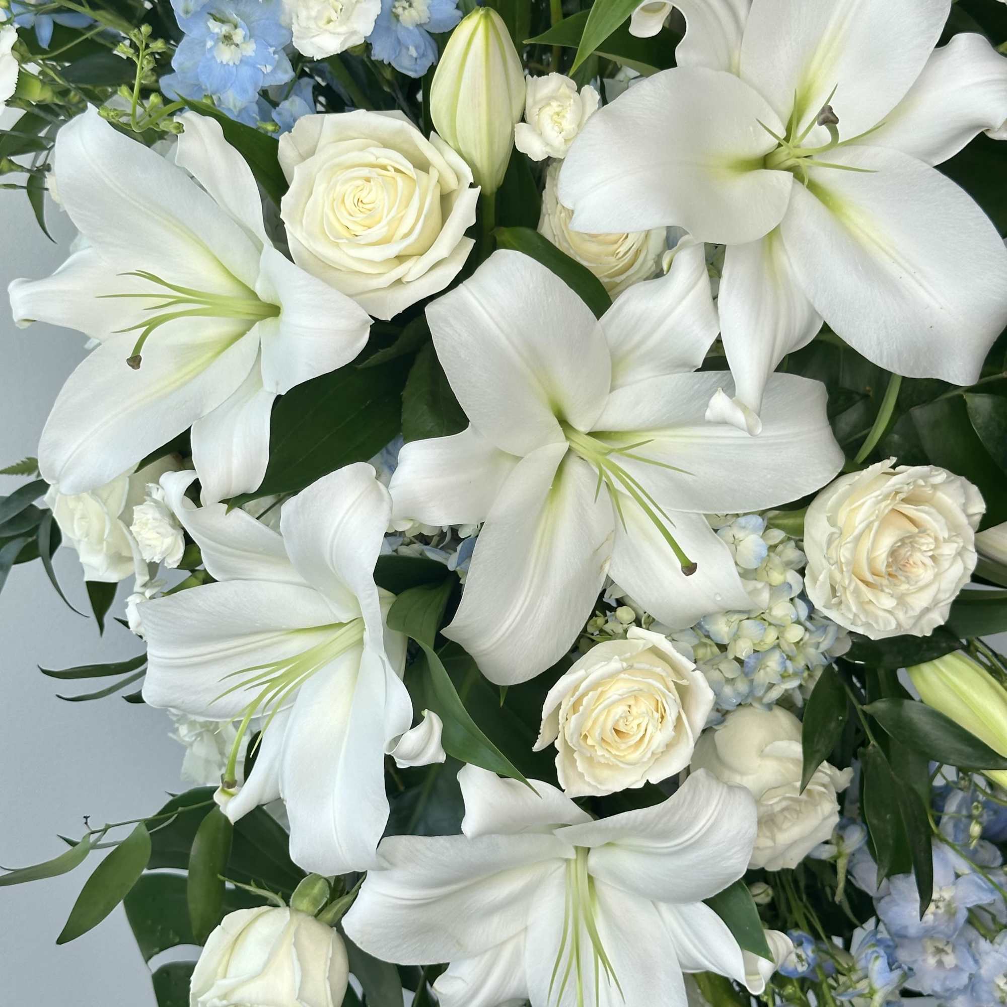 White lilies and cream roses with blue flowers in a bouquet