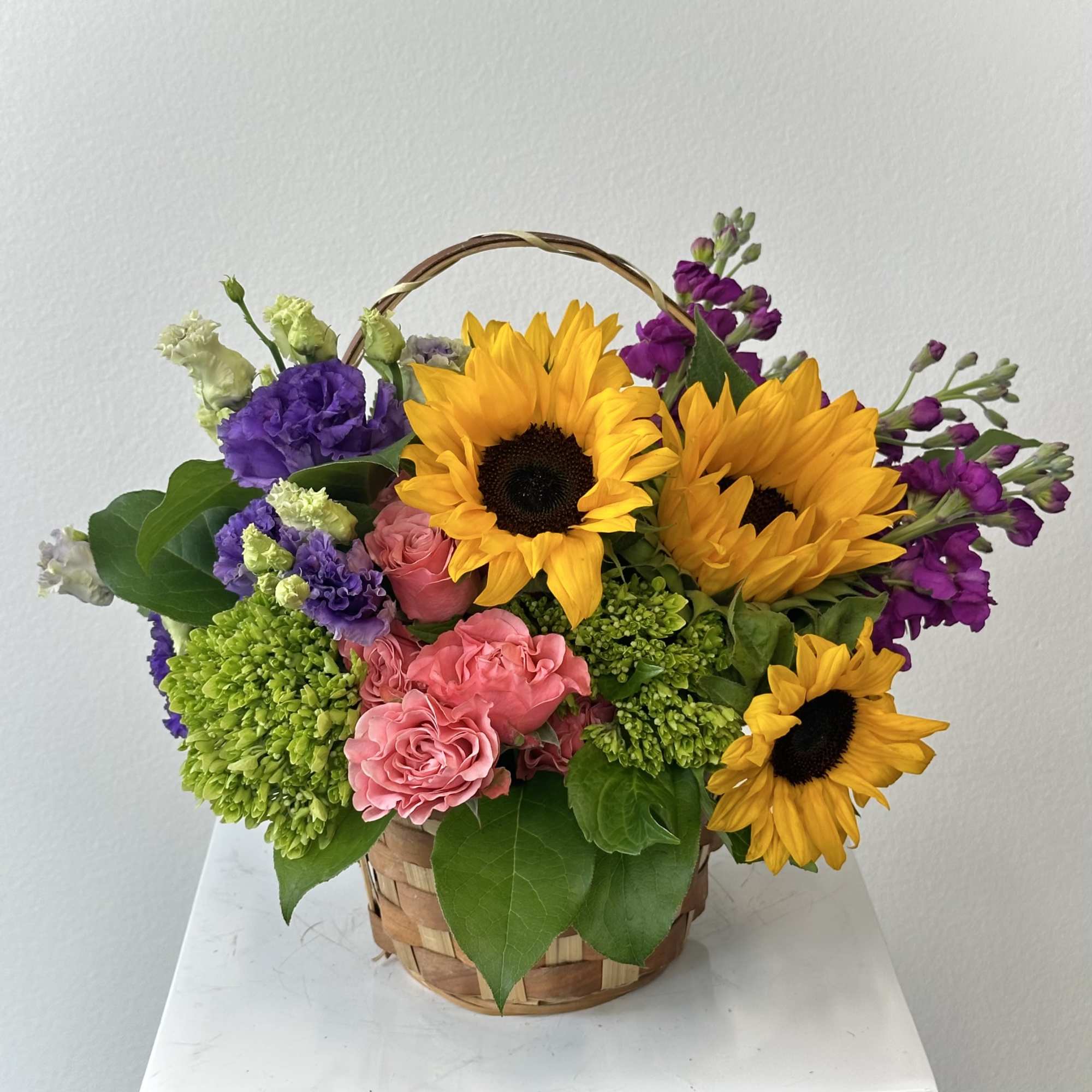 Basket arrangement with sunflowers, pink roses, and purple flowers