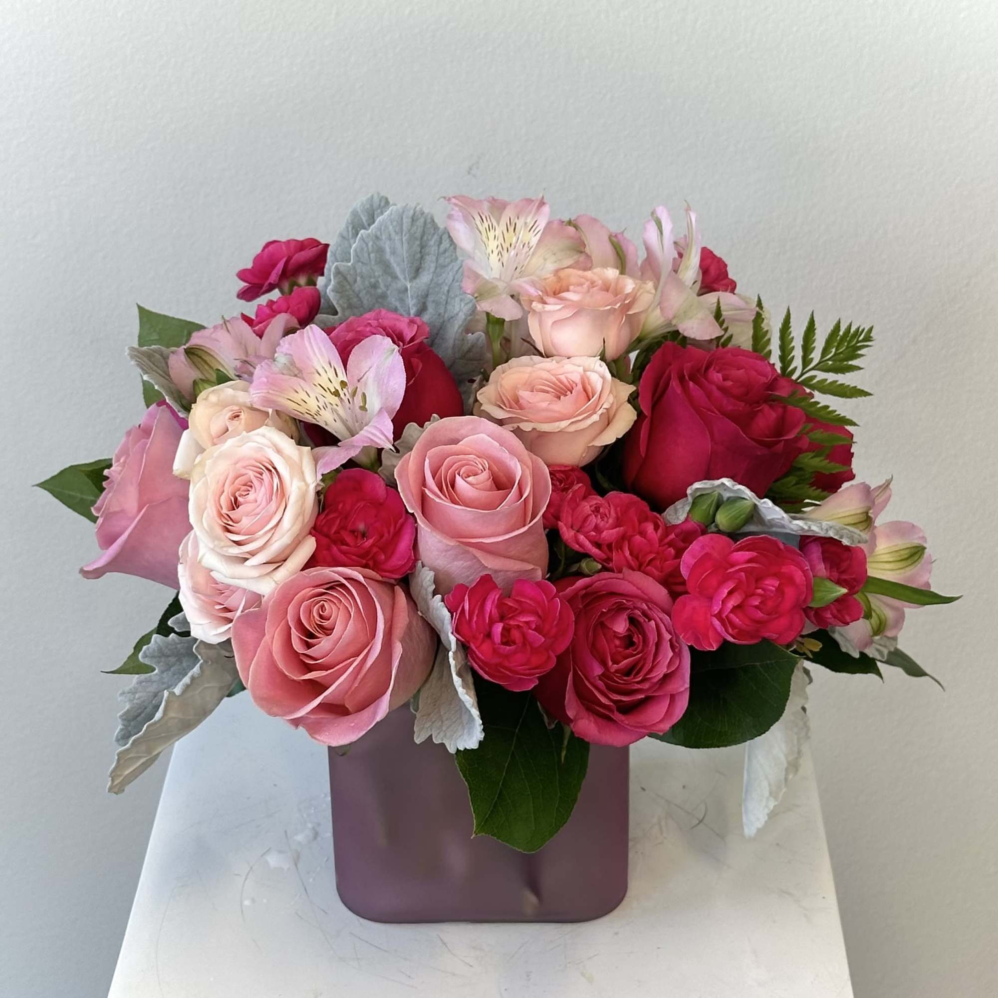 Pink and red rose arrangement with accent blooms in a mauve cube vase