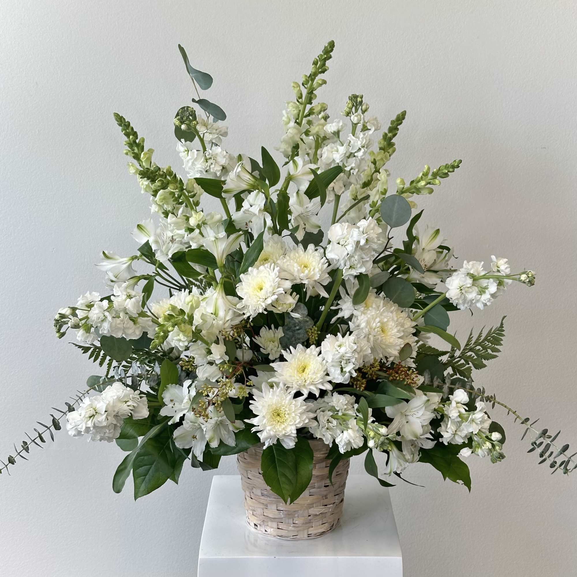 White floral arrangement in a woven basket with tall stems and greenery