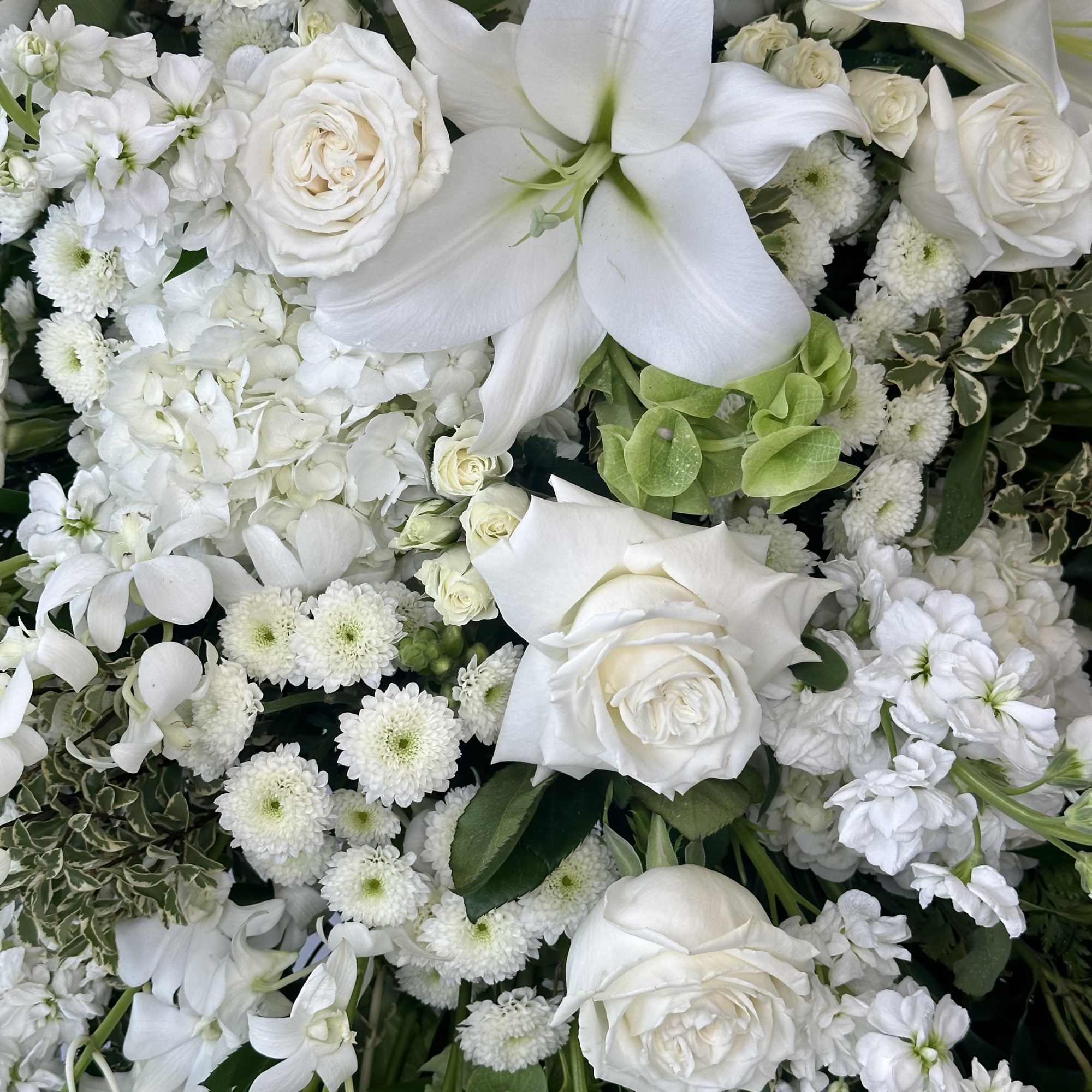 White roses and lilies mixed with small white blooms in a dense arrangement