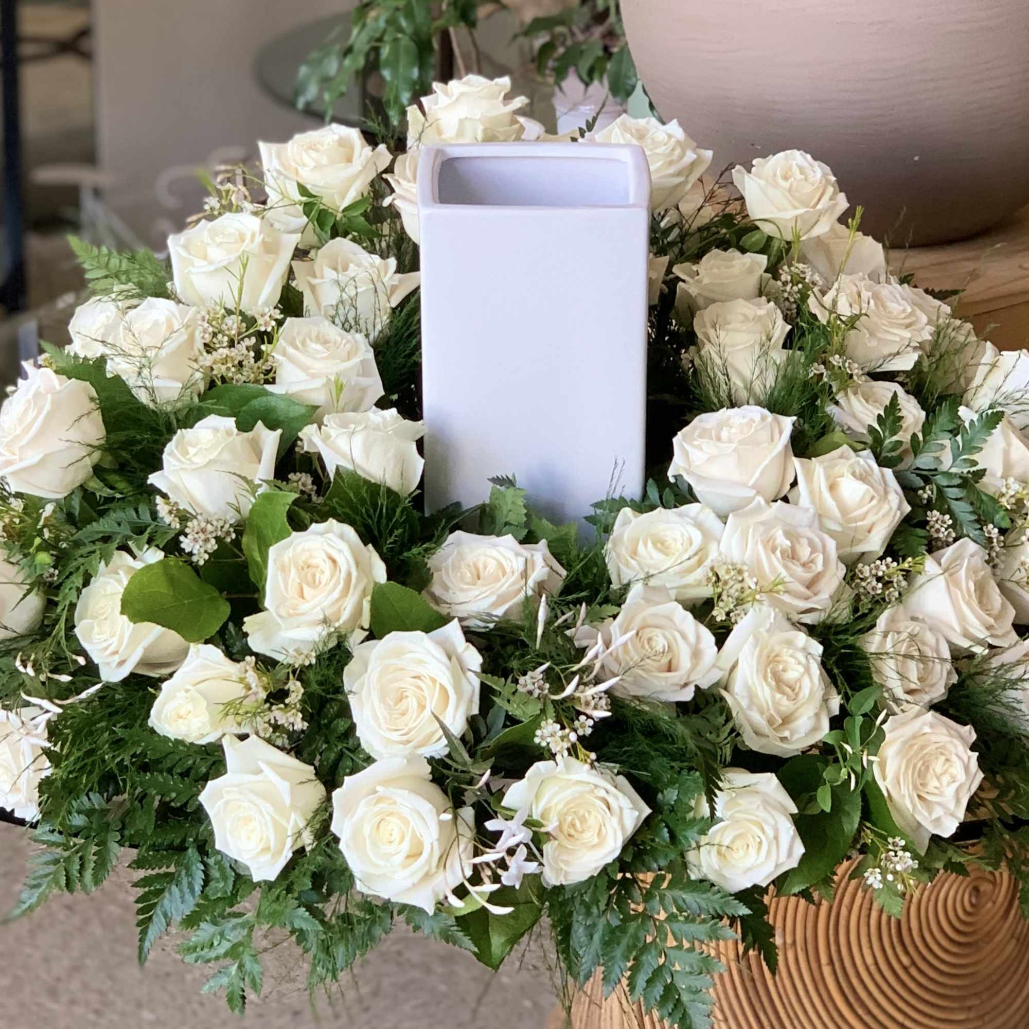 White rose wreath around a tall white vase centerpiece