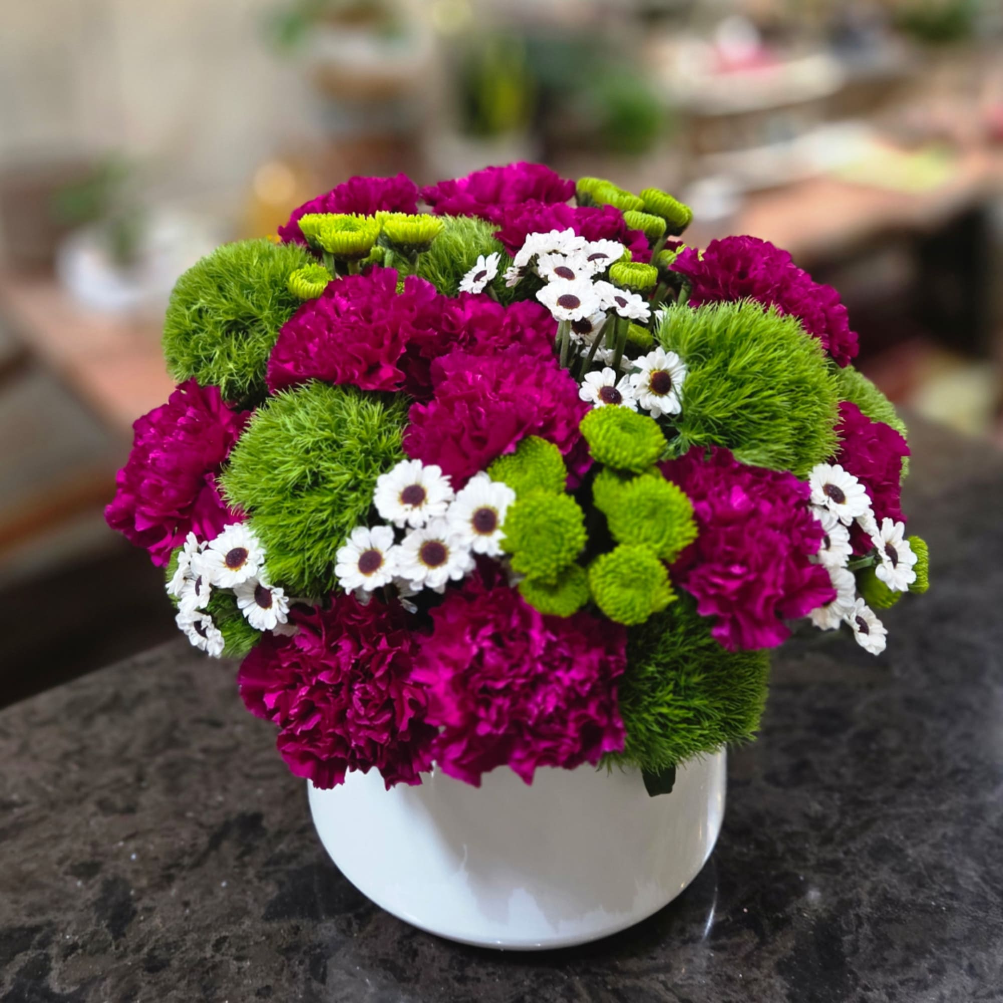 Magenta and green floral arrangement in a white vase with small white daisies, photo 2 of 2