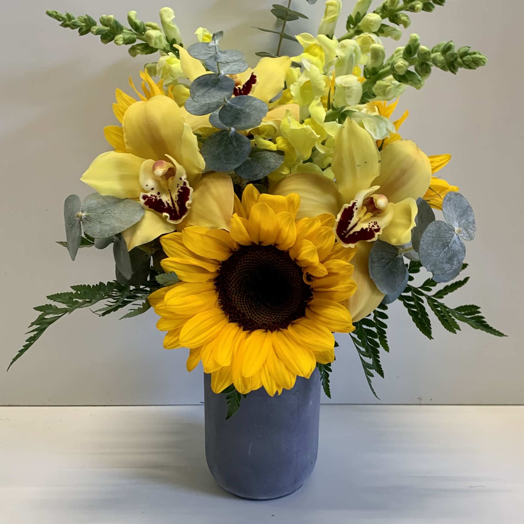 Sunflower and yellow orchid arrangement in a blue vase