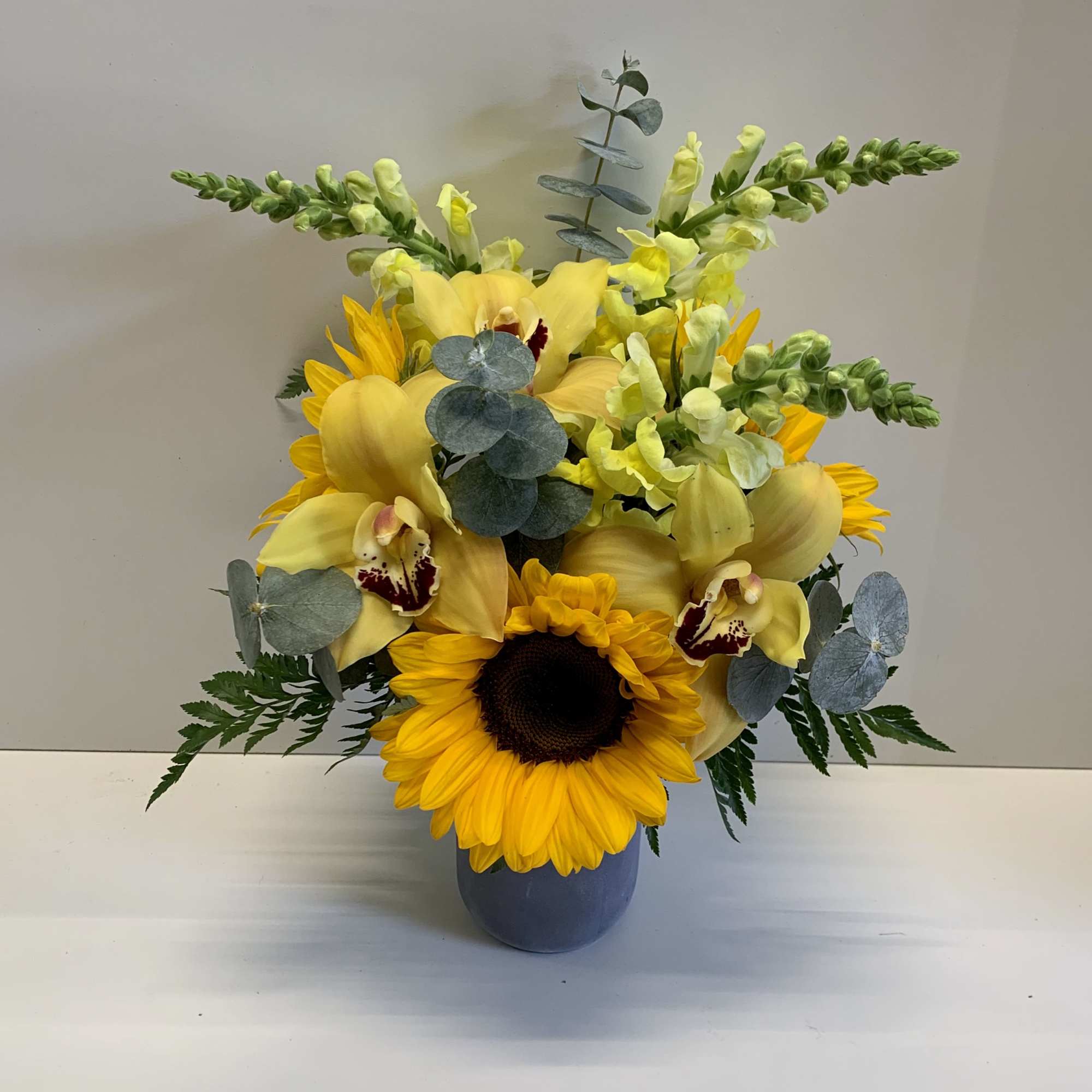 Yellow floral arrangement in a blue vase with a sunflower and orchids