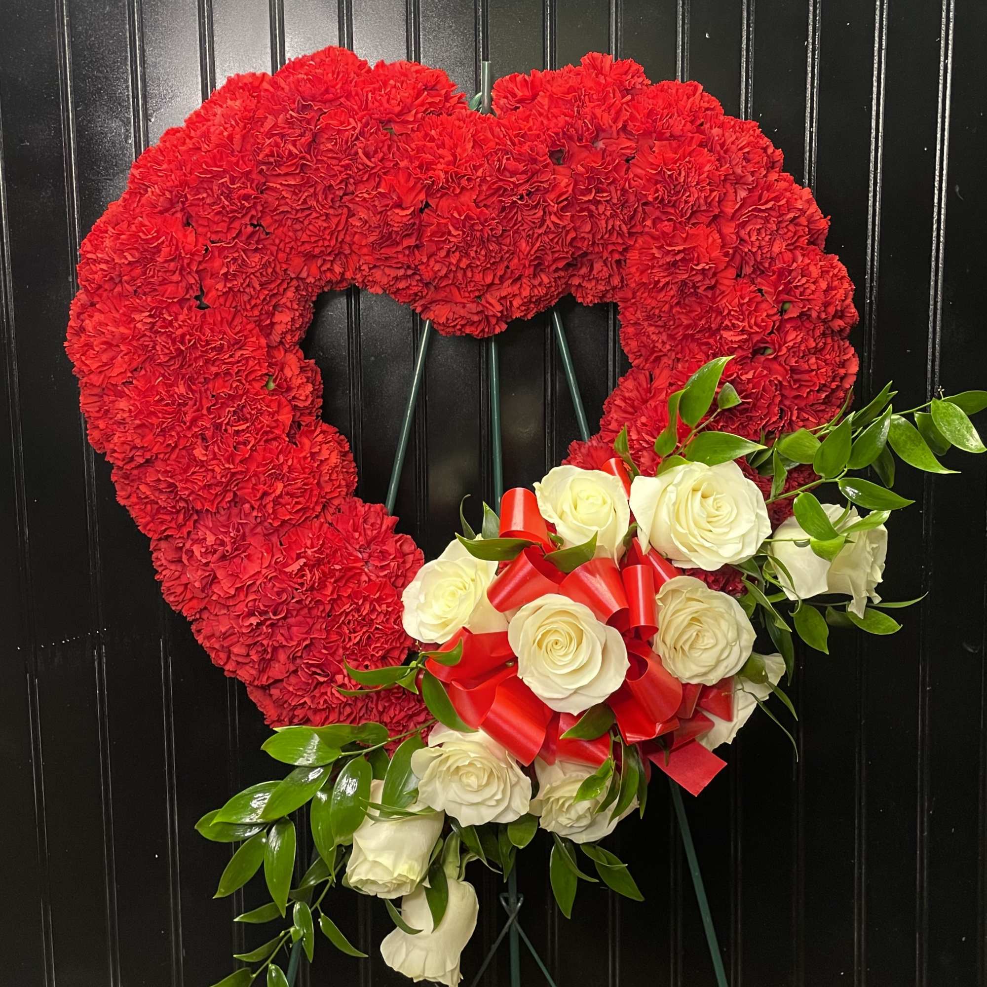 Heart-shaped red carnation wreath with white roses and a red ribbon bow
