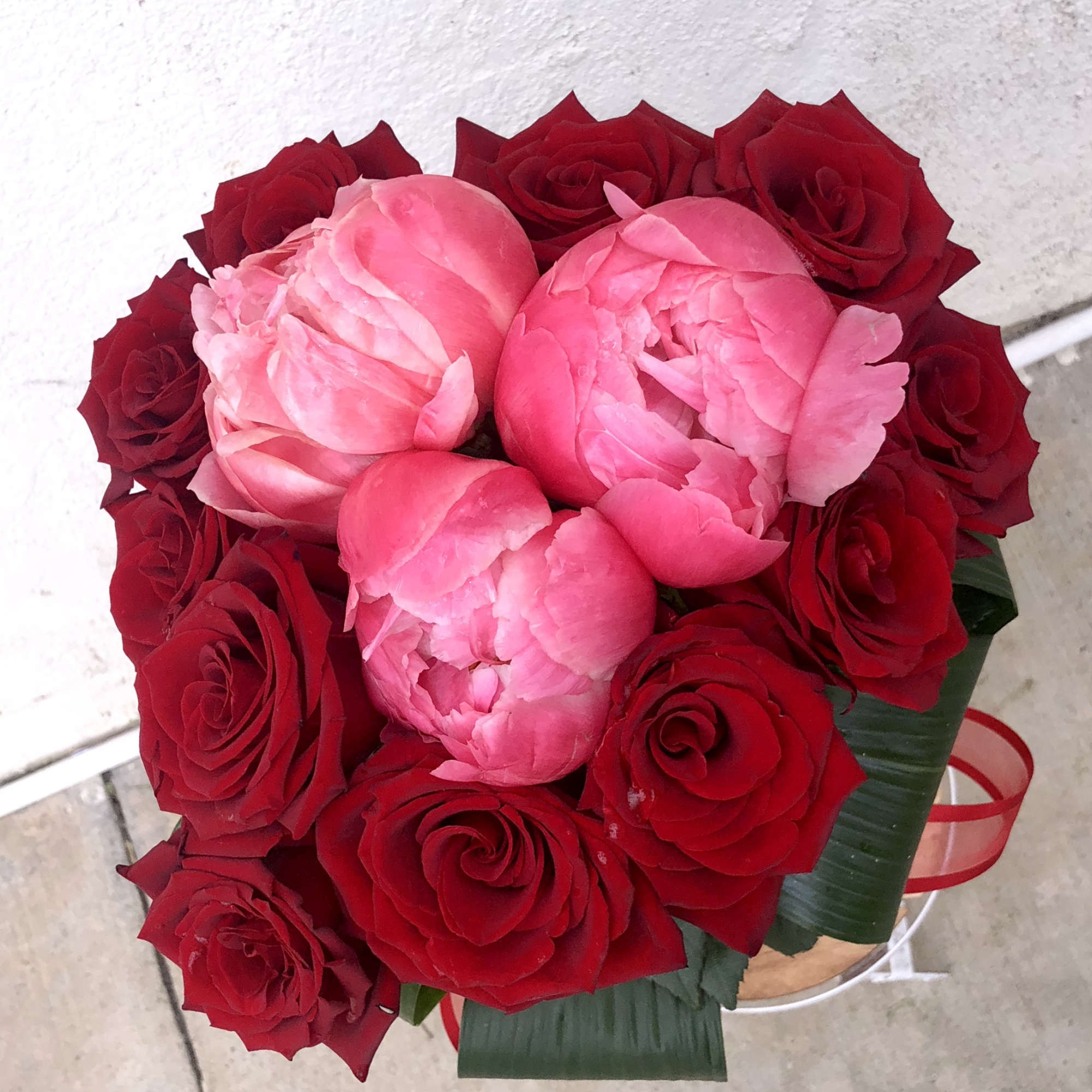 Bouquet of red roses and pink peonies in a round box
