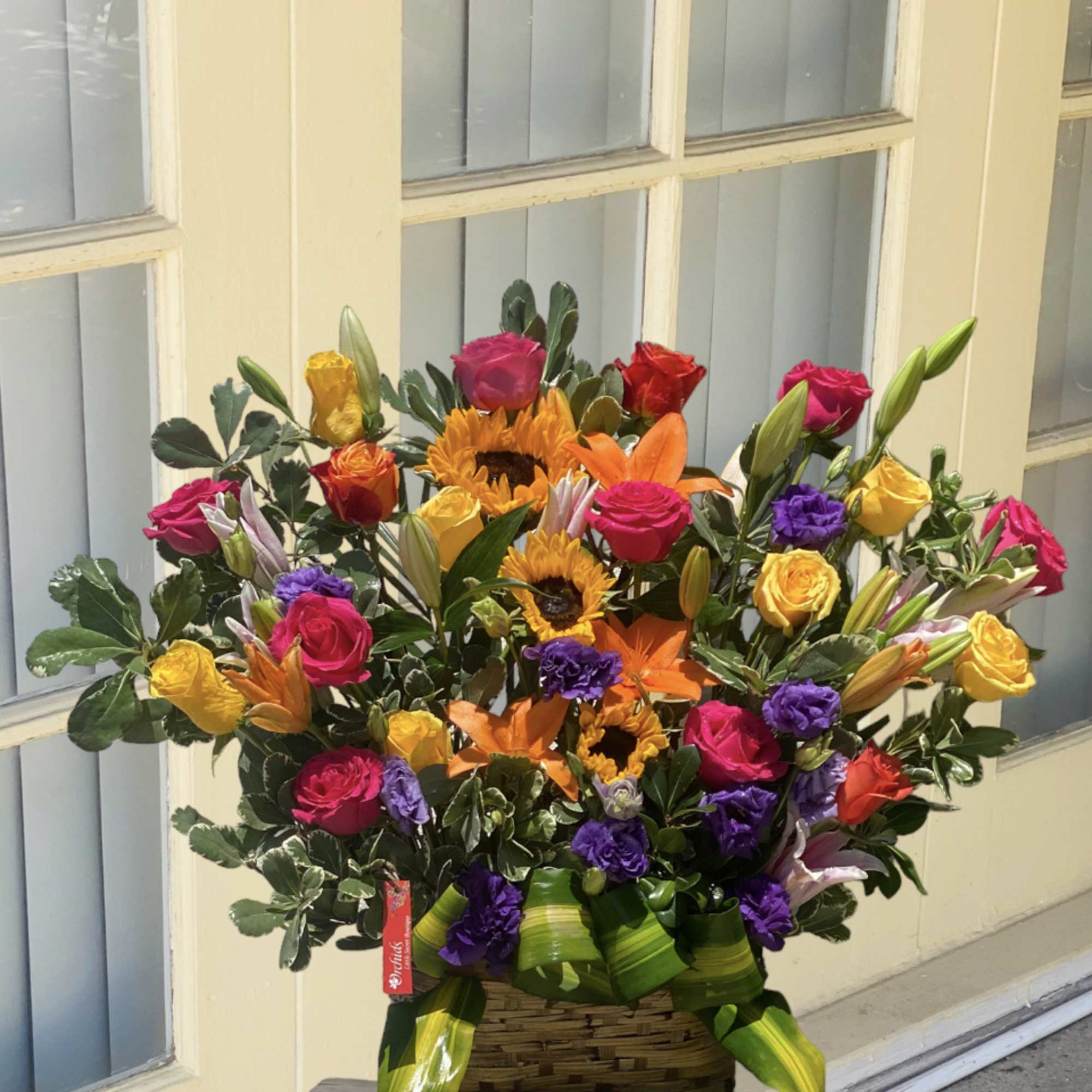 Colorful bouquet with roses, sunflowers, lilies, and purple blooms in a basket