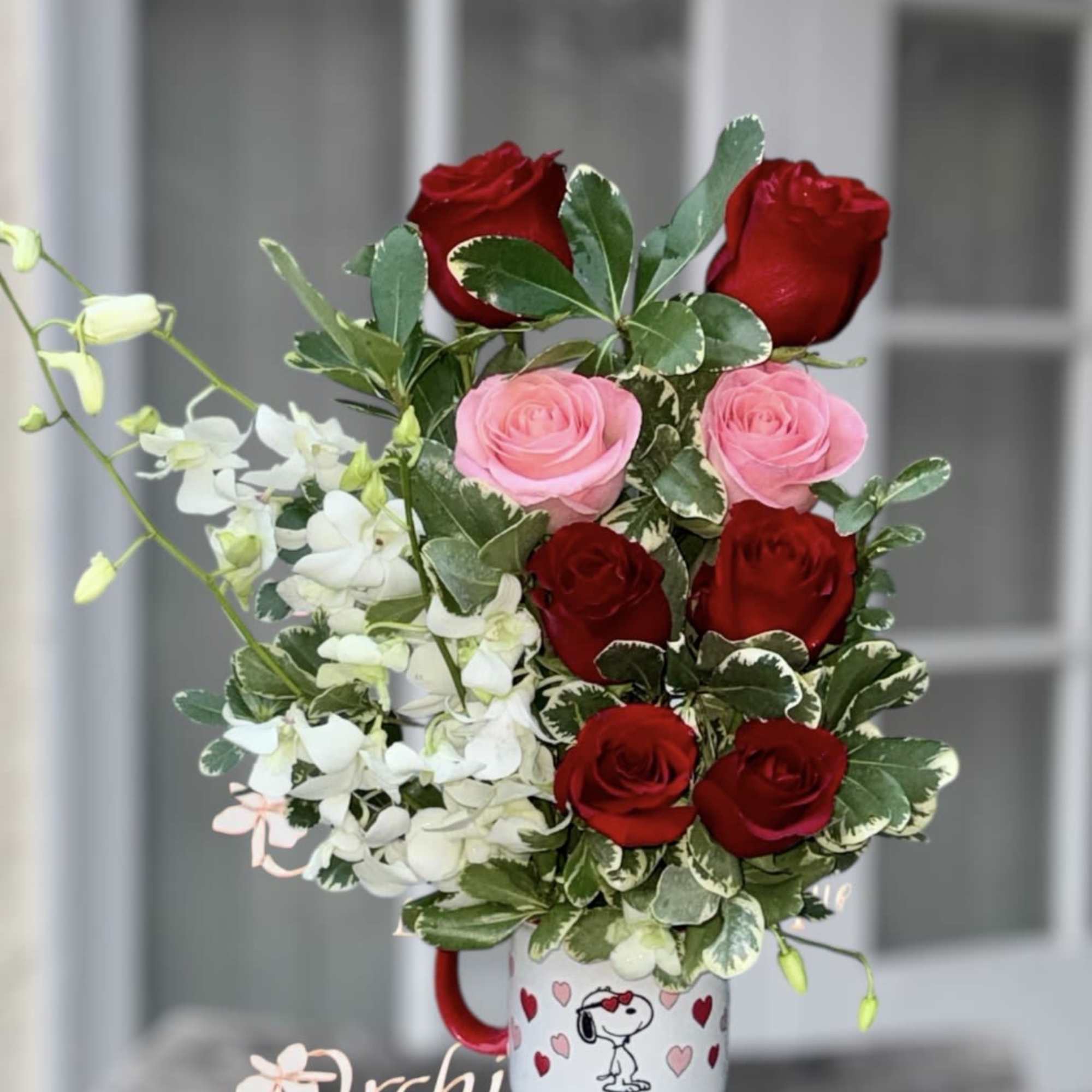 Bouquet of red and pink roses with white orchids in a Snoopy mug
