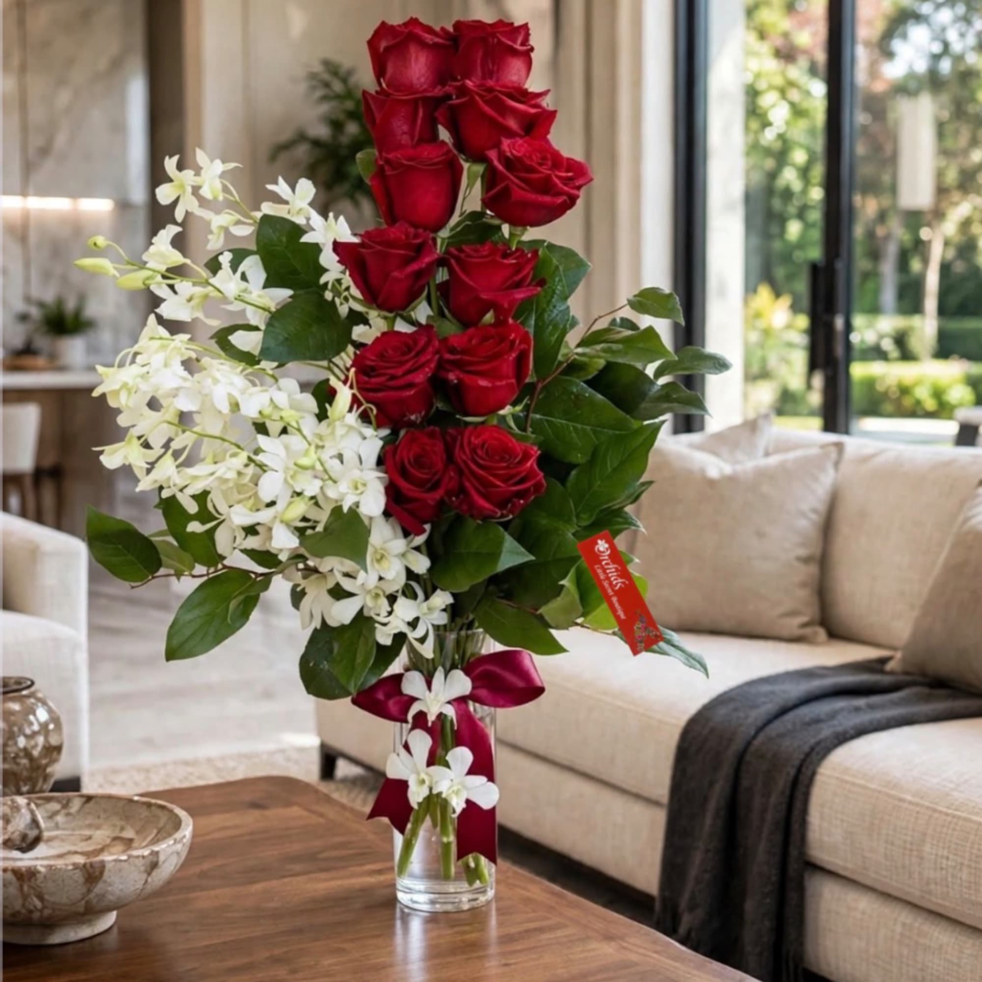 Tall arrangement of red roses and white orchids in a clear glass vase
