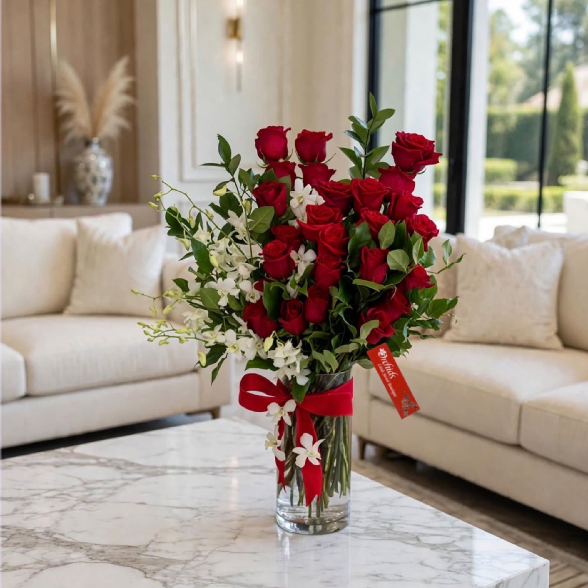 Red roses and white orchids arranged in a glass vase with a red ribbon.
