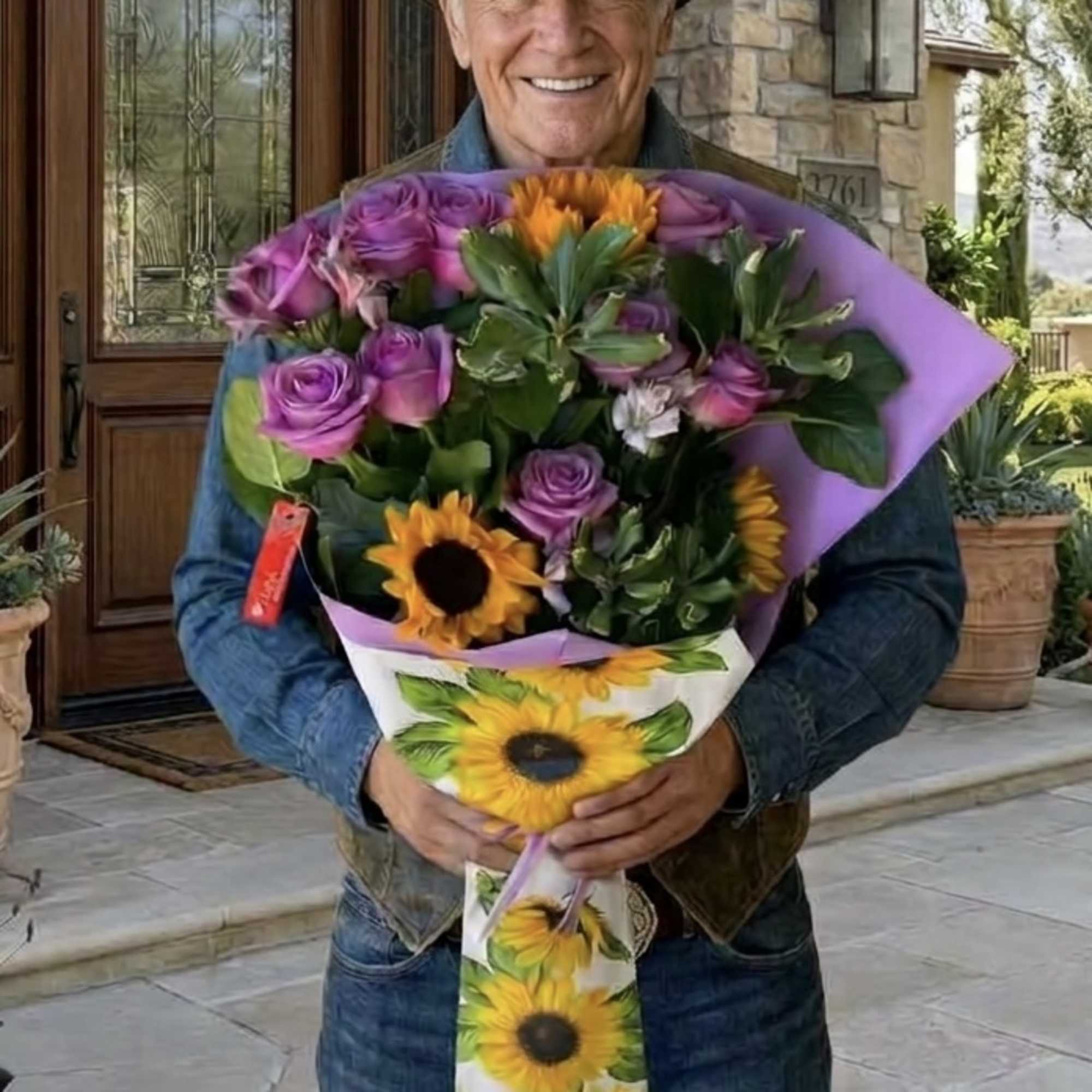 Man holding a bouquet of purple roses and sunflowers wrapped in purple paper