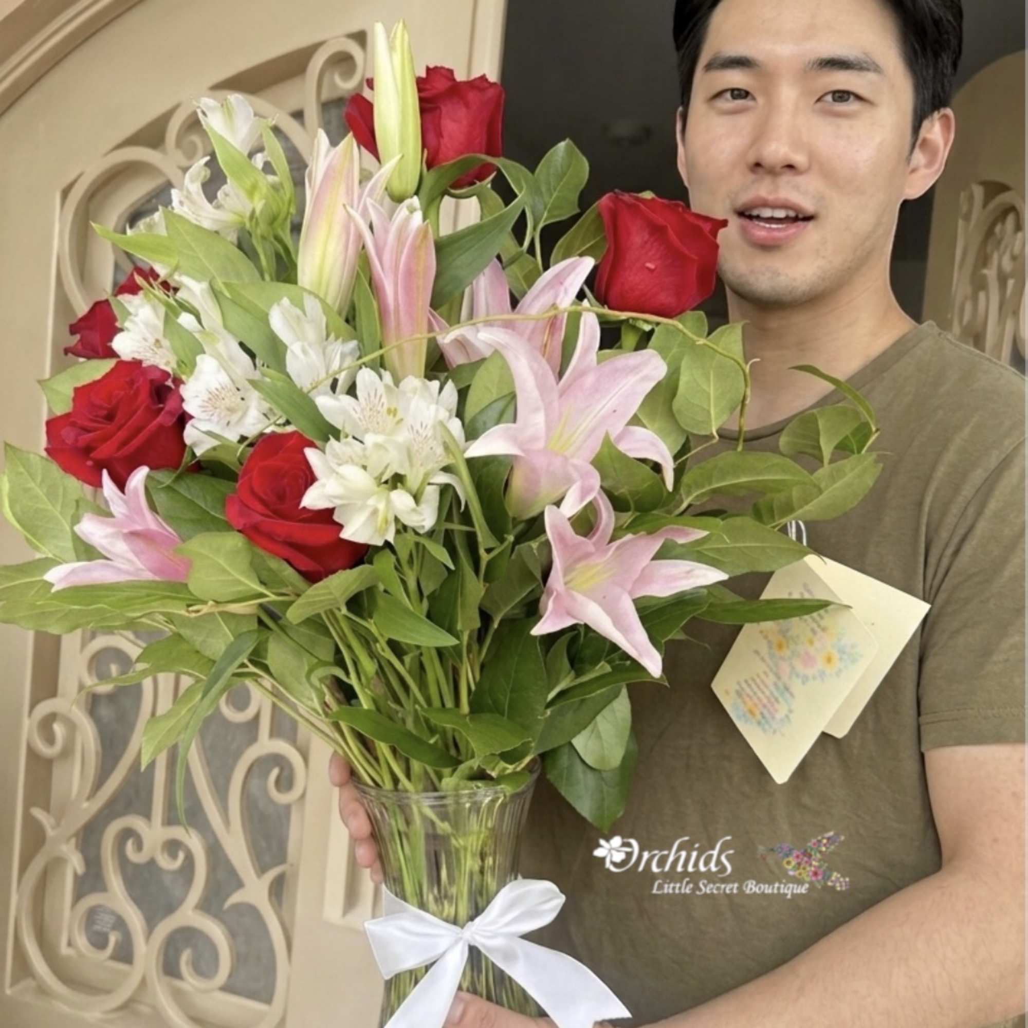 Man holding a bouquet of red roses, pink lilies, and white flowers in a glass vase