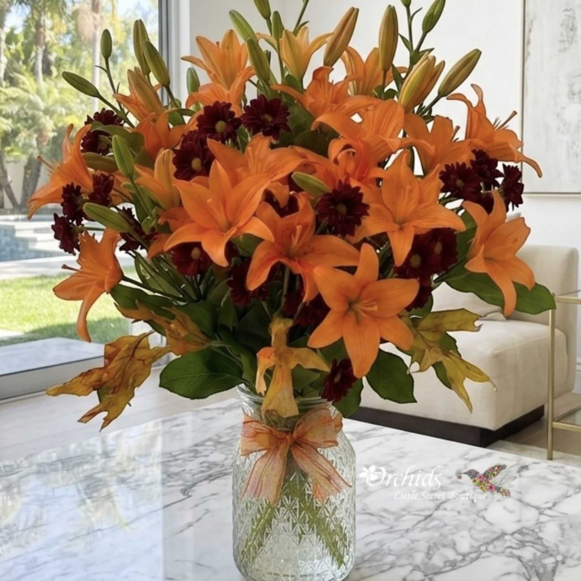 Orange lilies and dark burgundy mums in a glass vase with a ribbon