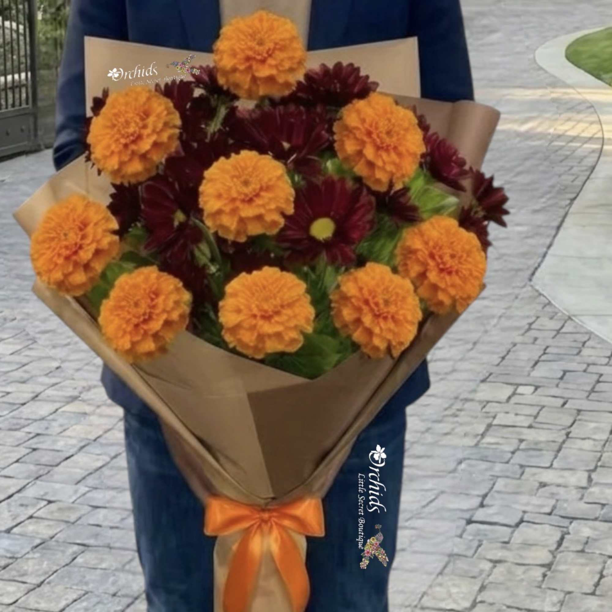 Bouquet of orange marigolds and dark red daisies wrapped in brown paper