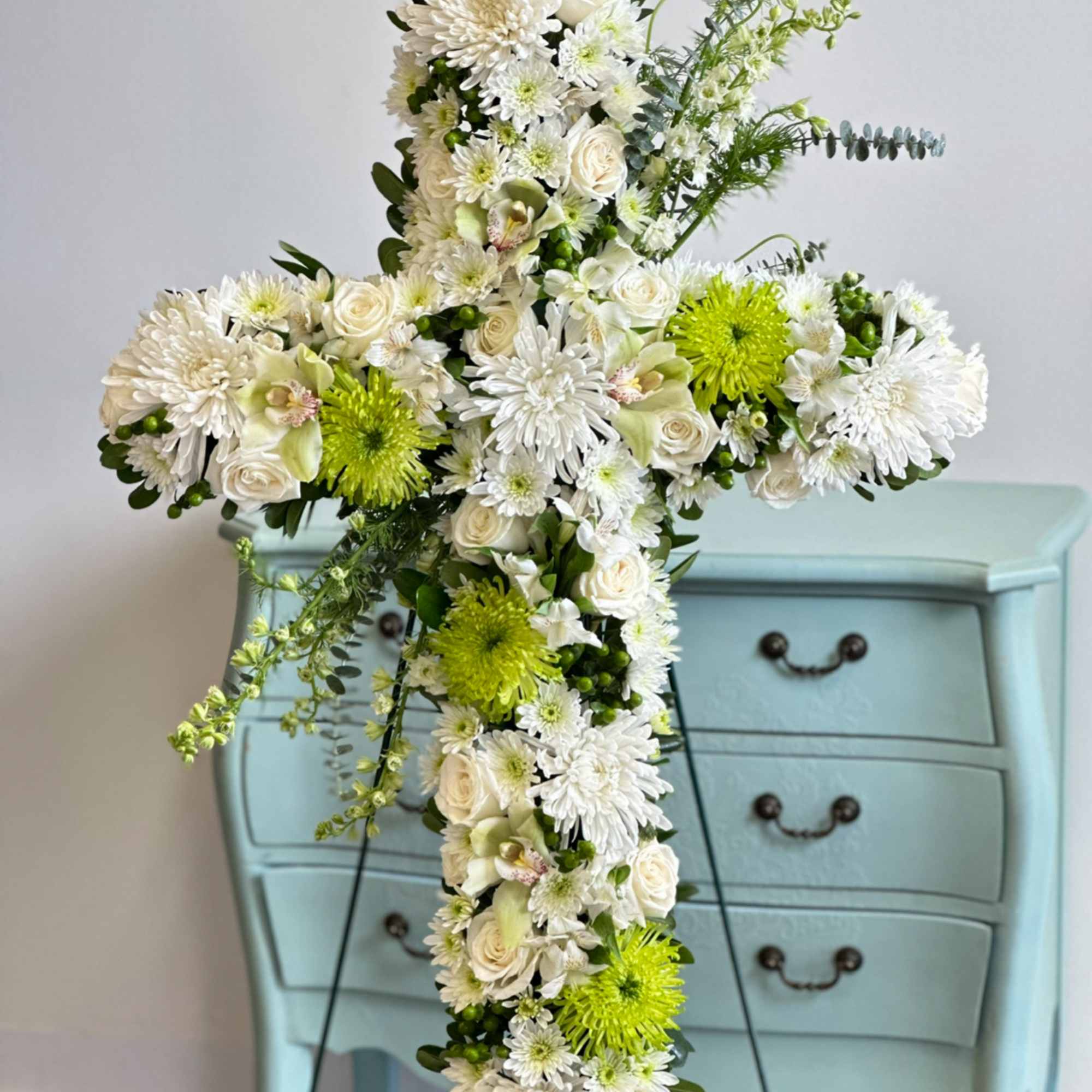 White floral cross arrangement with green accents on a stand