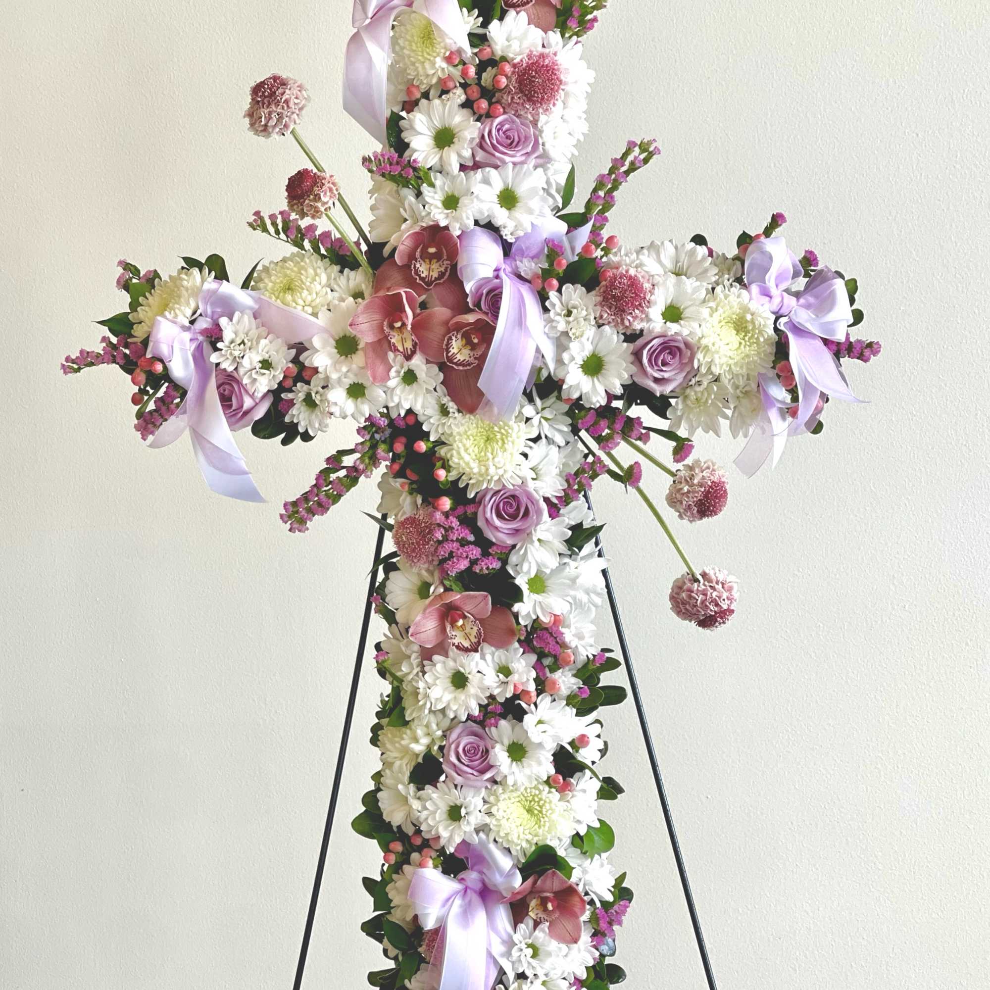 Cross-shaped floral arrangement with pink and white flowers on a stand