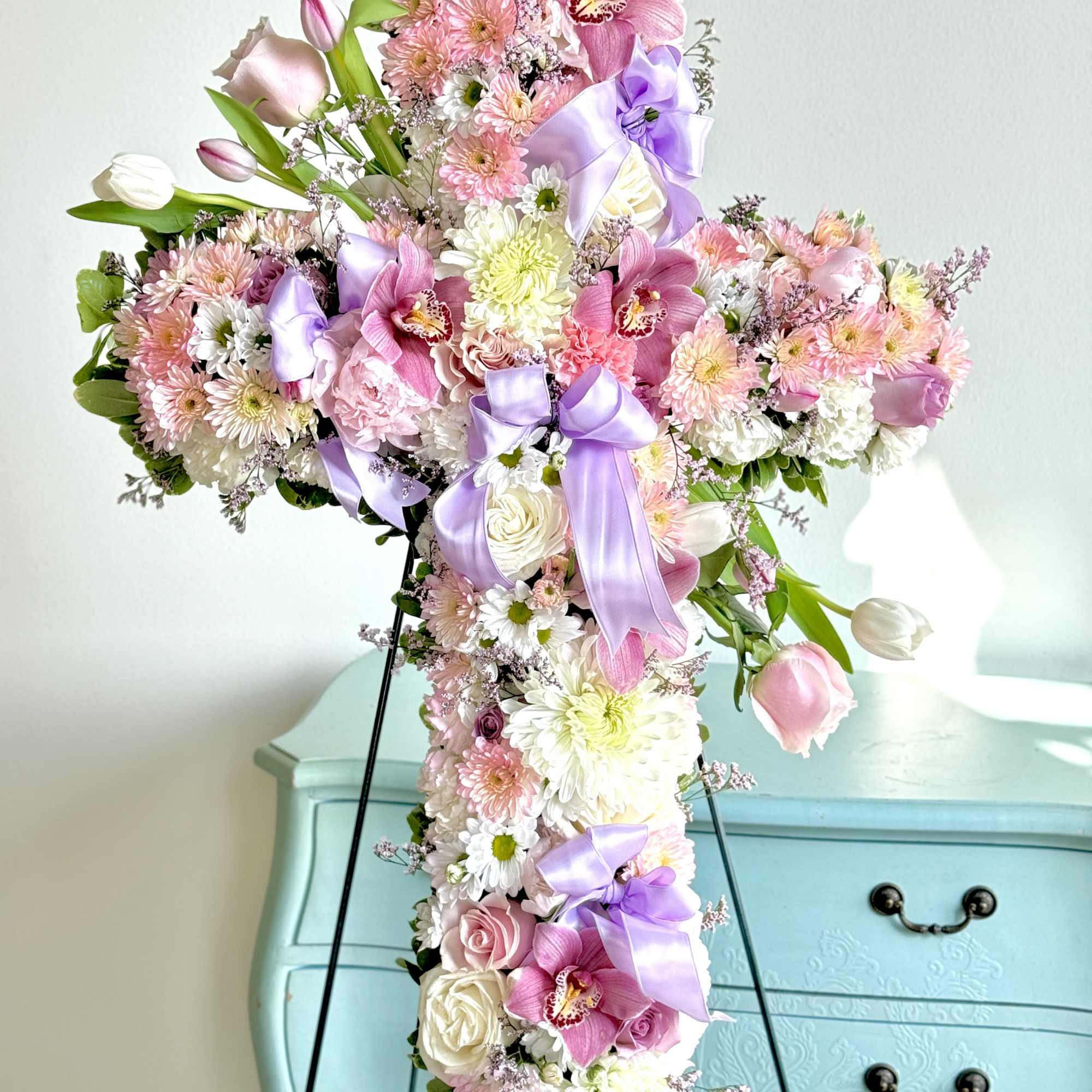 Cross-shaped floral arrangement with pink, white, and lavender blooms on a stand