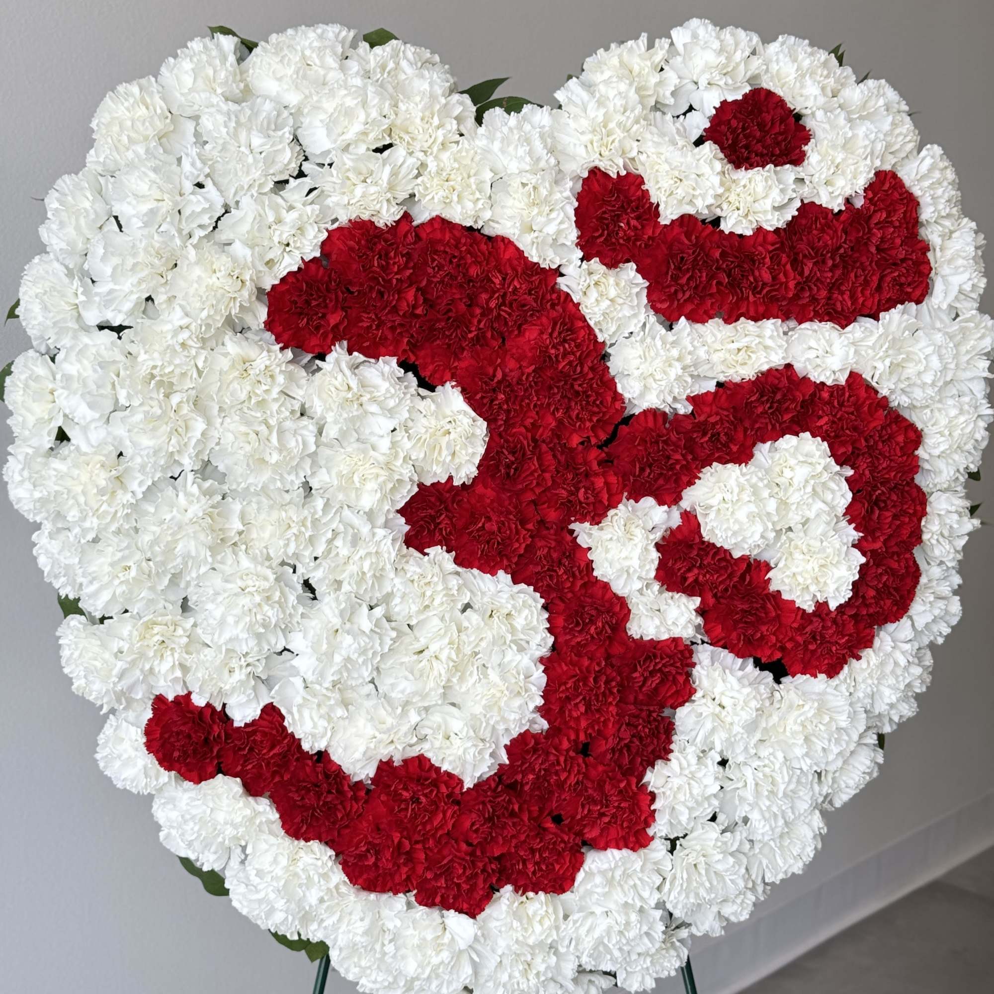 Heart-shaped floral tribute of red and white carnations on a stand