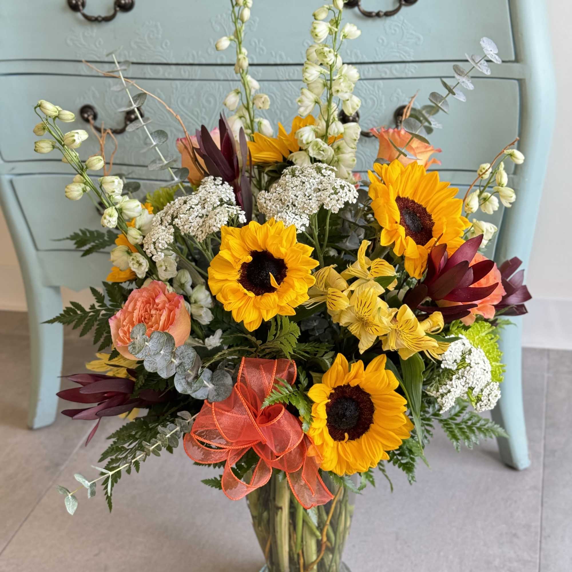Mixed bouquet with sunflowers, roses, and white filler flowers in a glass vase.