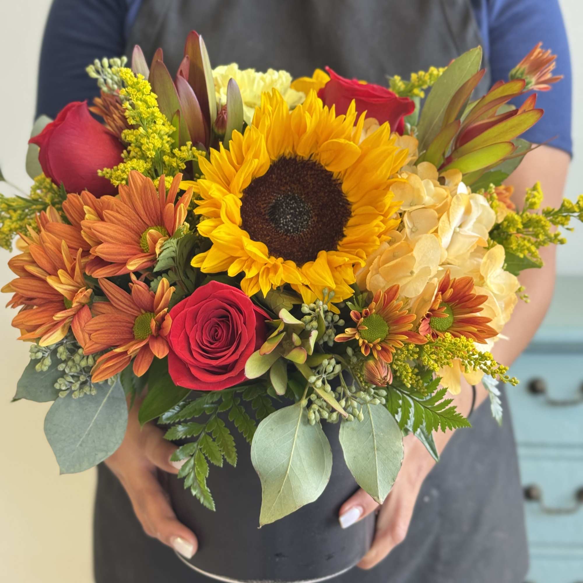 Mixed bouquet with a sunflower, red roses, and orange daisies in a black container