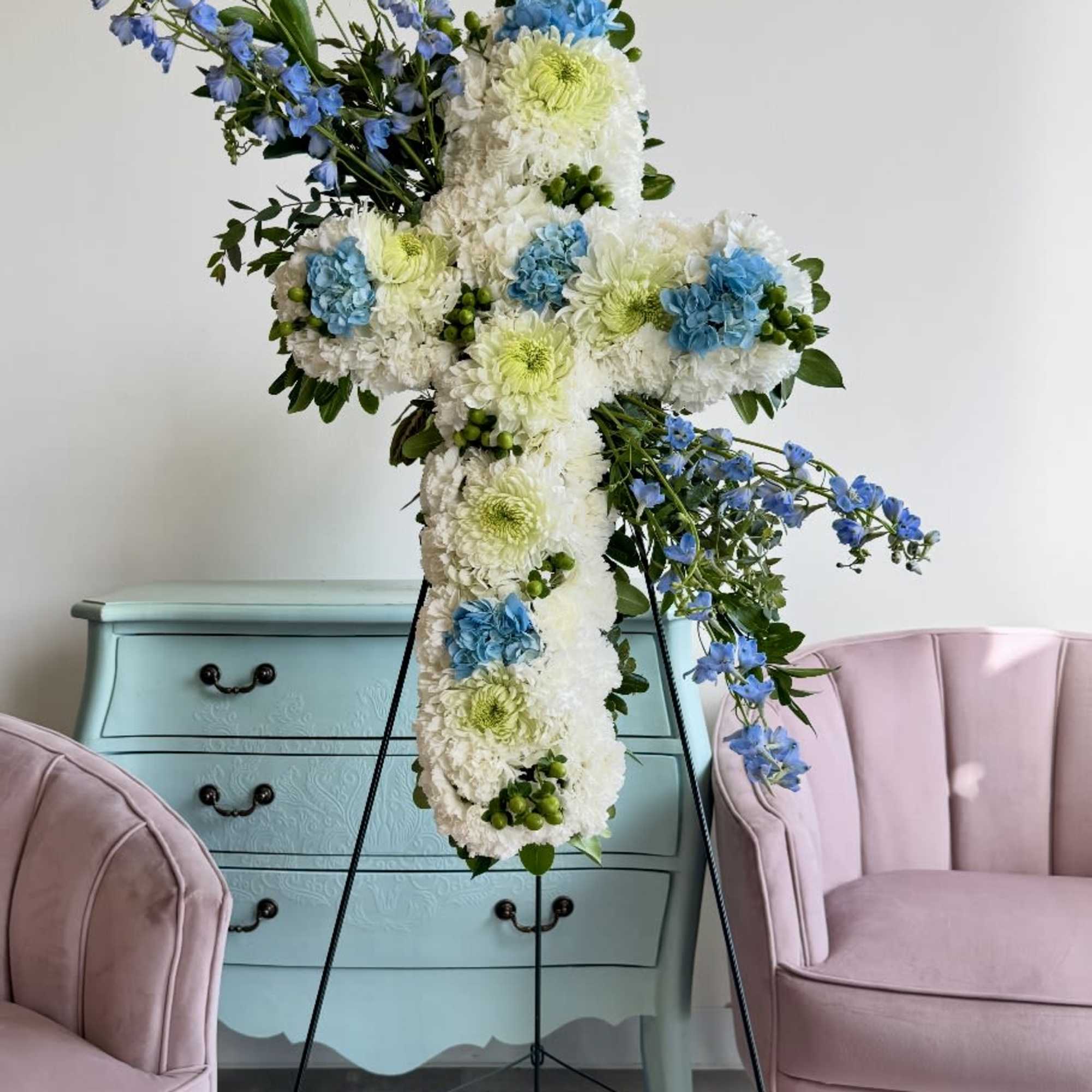 Large floral cross on a stand with white, blue, and green flowers