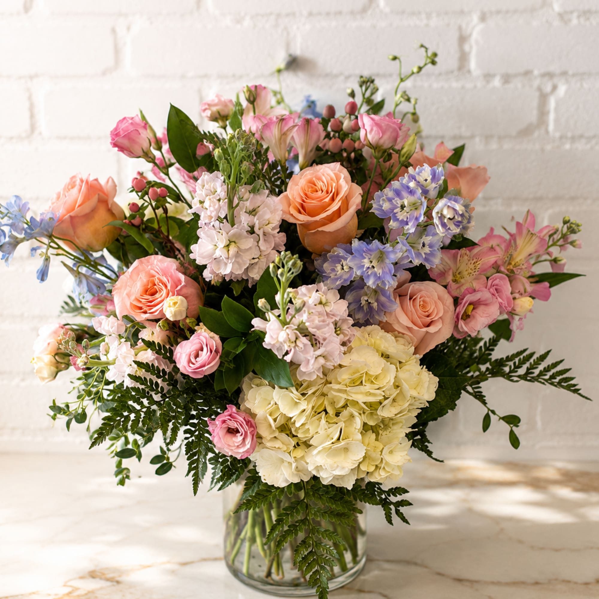 Mixed bouquet of pink, peach, lavender, and white flowers in a glass vase