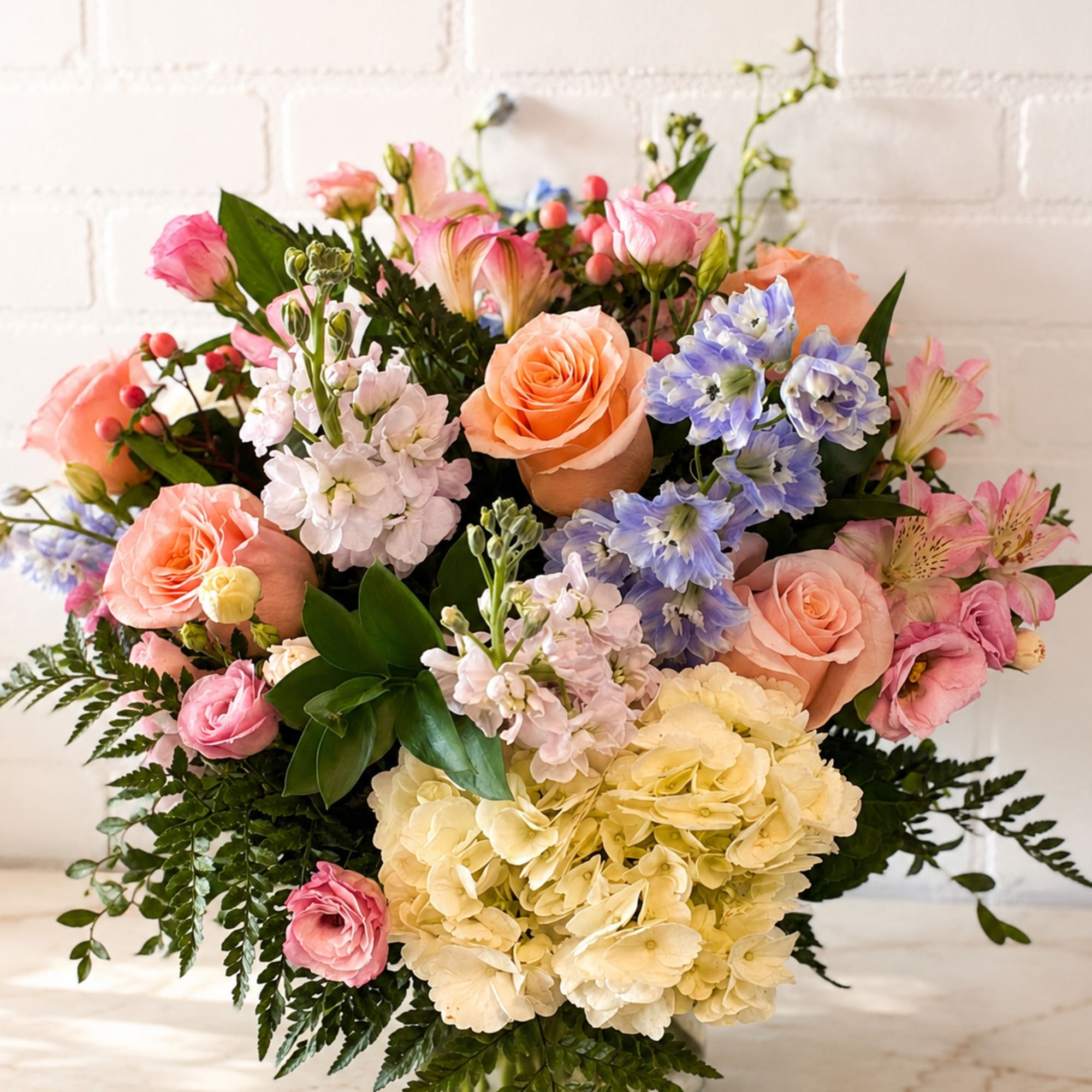 Mixed bouquet of pink and peach roses with blue and cream flowers in a glass vase