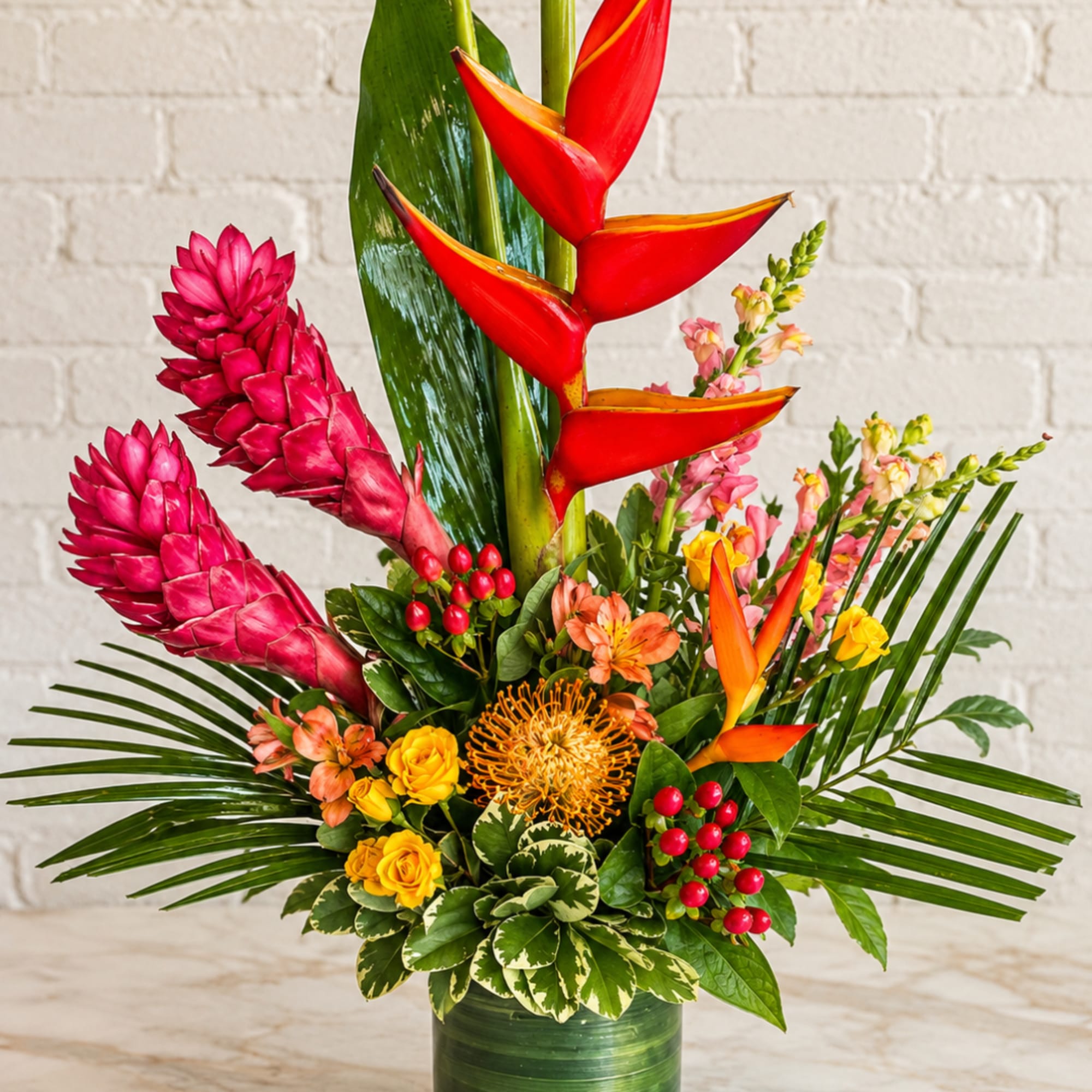 Tropical flower arrangement with red heliconia and pink ginger in a green vase.