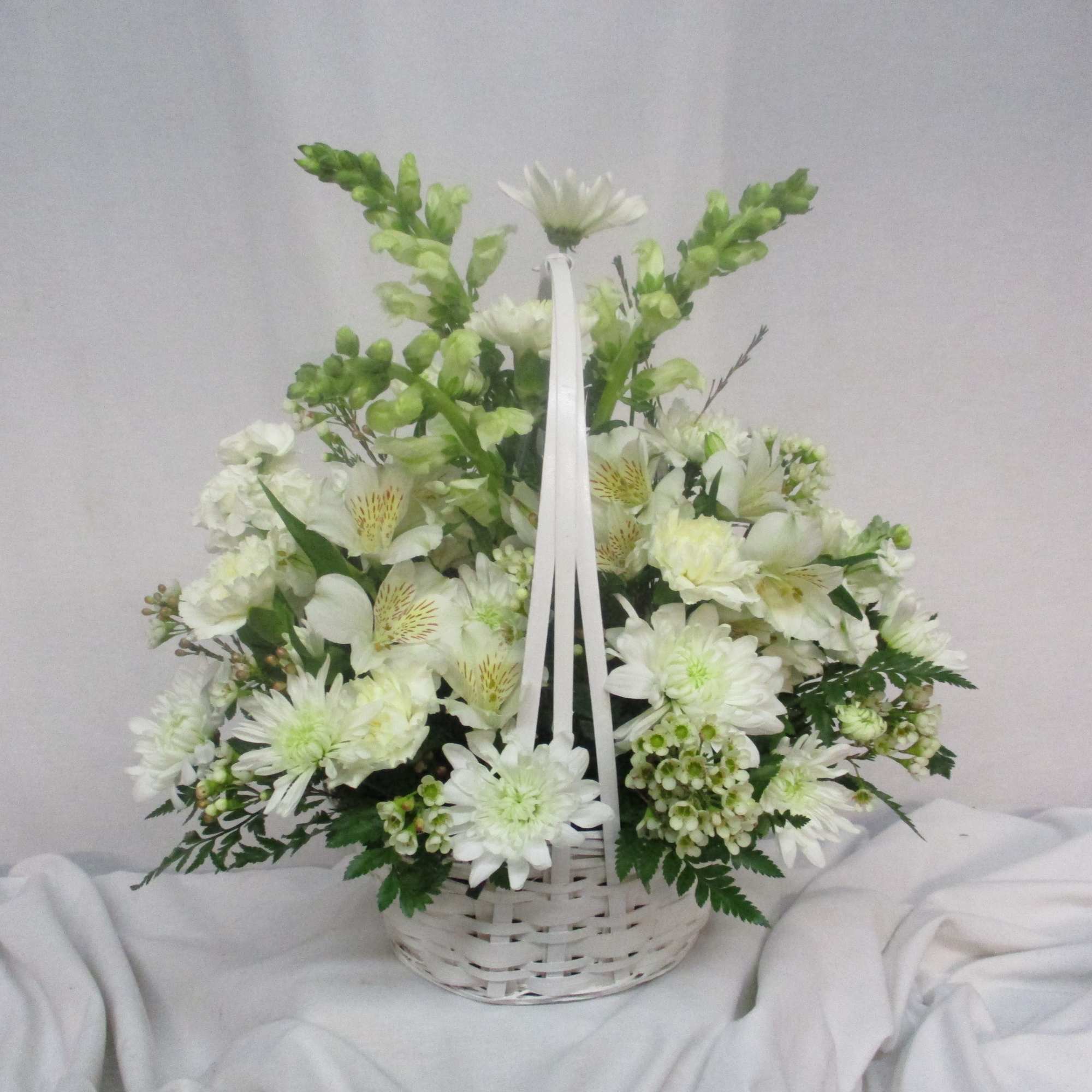 White floral arrangement in a white wicker basket with ribbon handles
