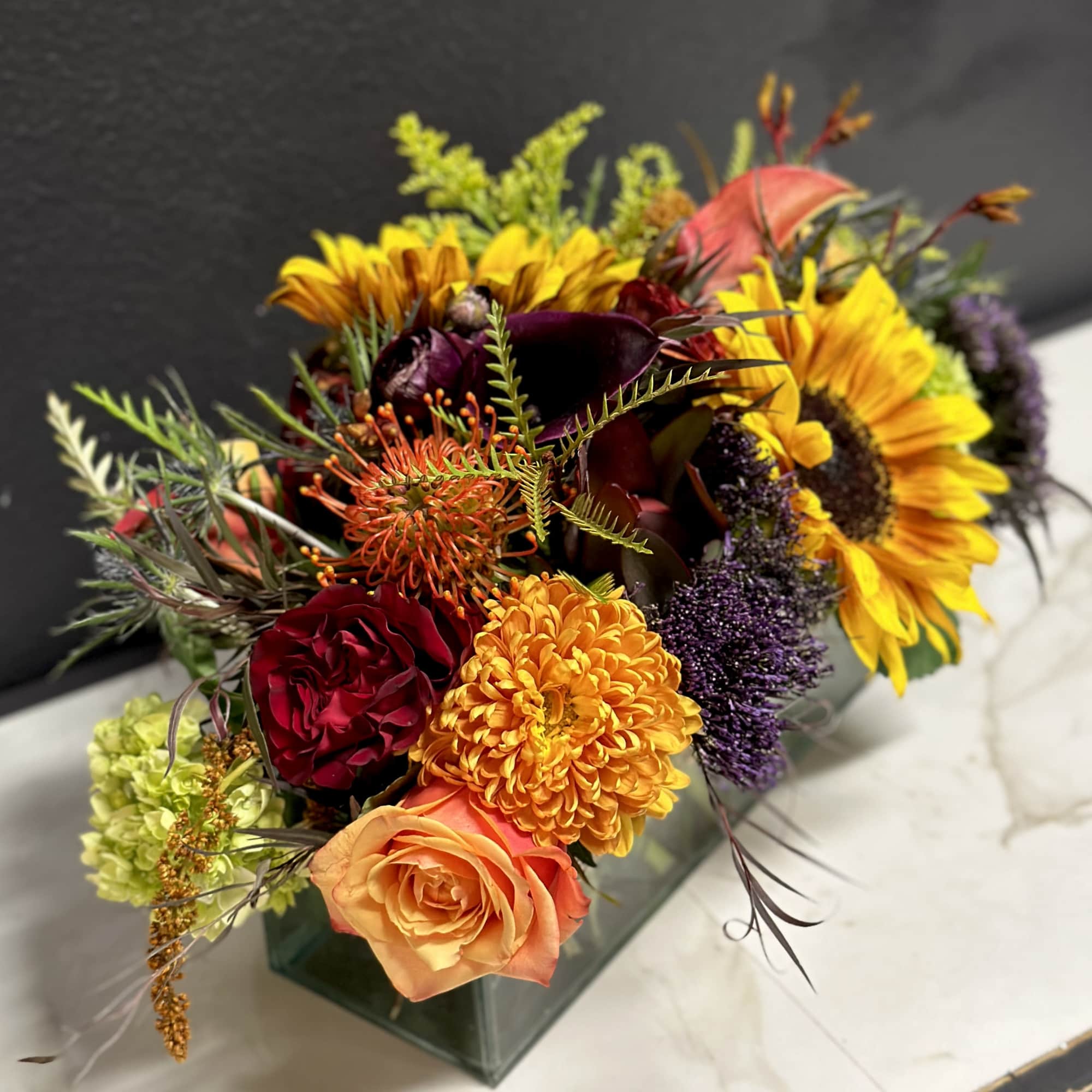 Mixed bouquet with sunflowers, roses, and mums in a square glass vase