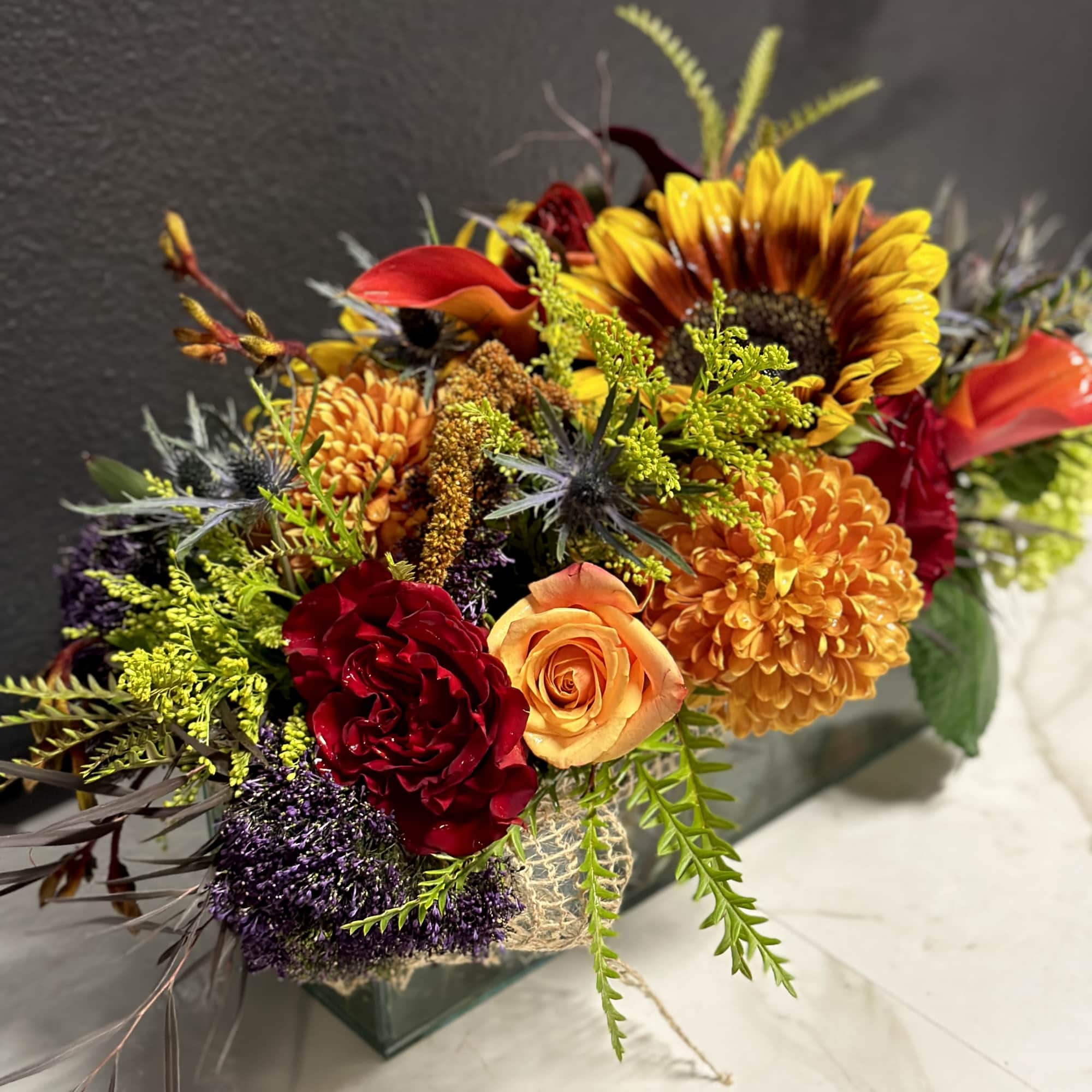 Mixed bouquet with sunflowers, roses, and orange mums in a glass vase