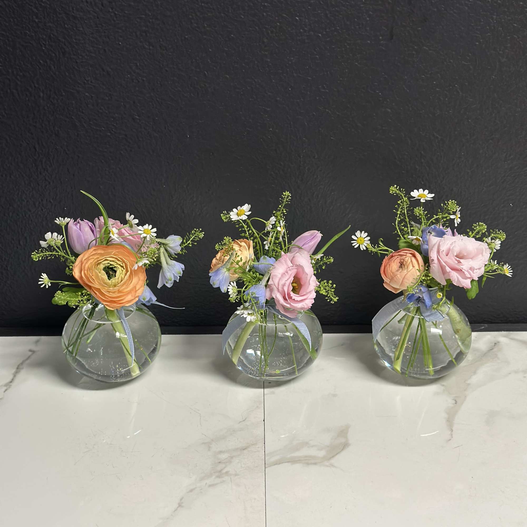 A trio of budvases filled with seasonal blooms in soft pastel shades.