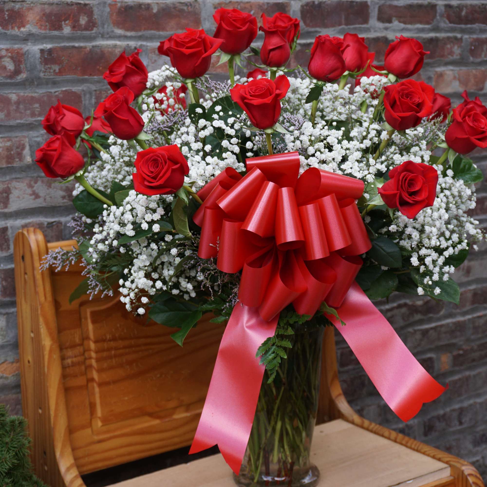 Red roses in a glass vase with white baby's breath and a red bow