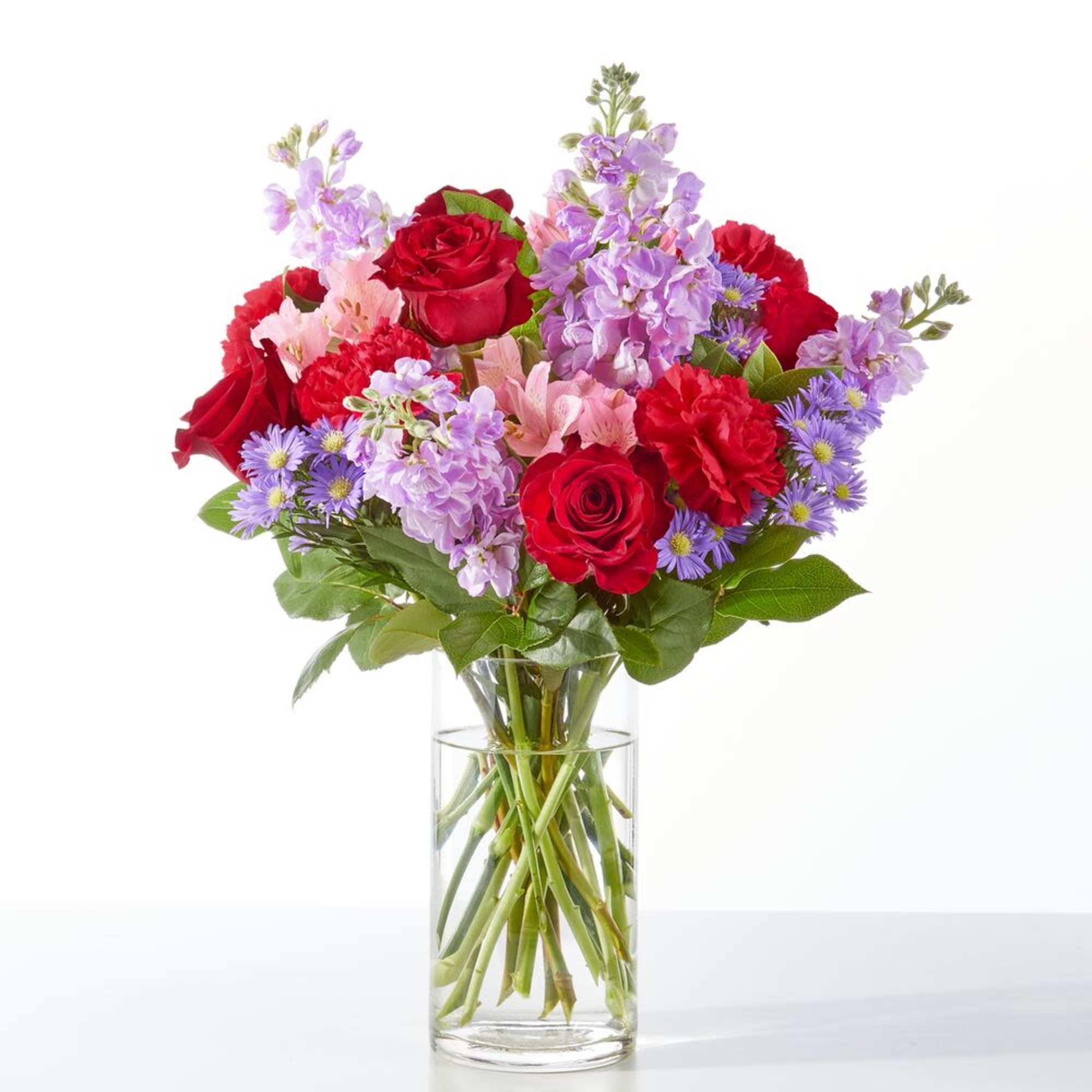 Bouquet of red roses, purple flowers, and pink blooms in a clear glass vase