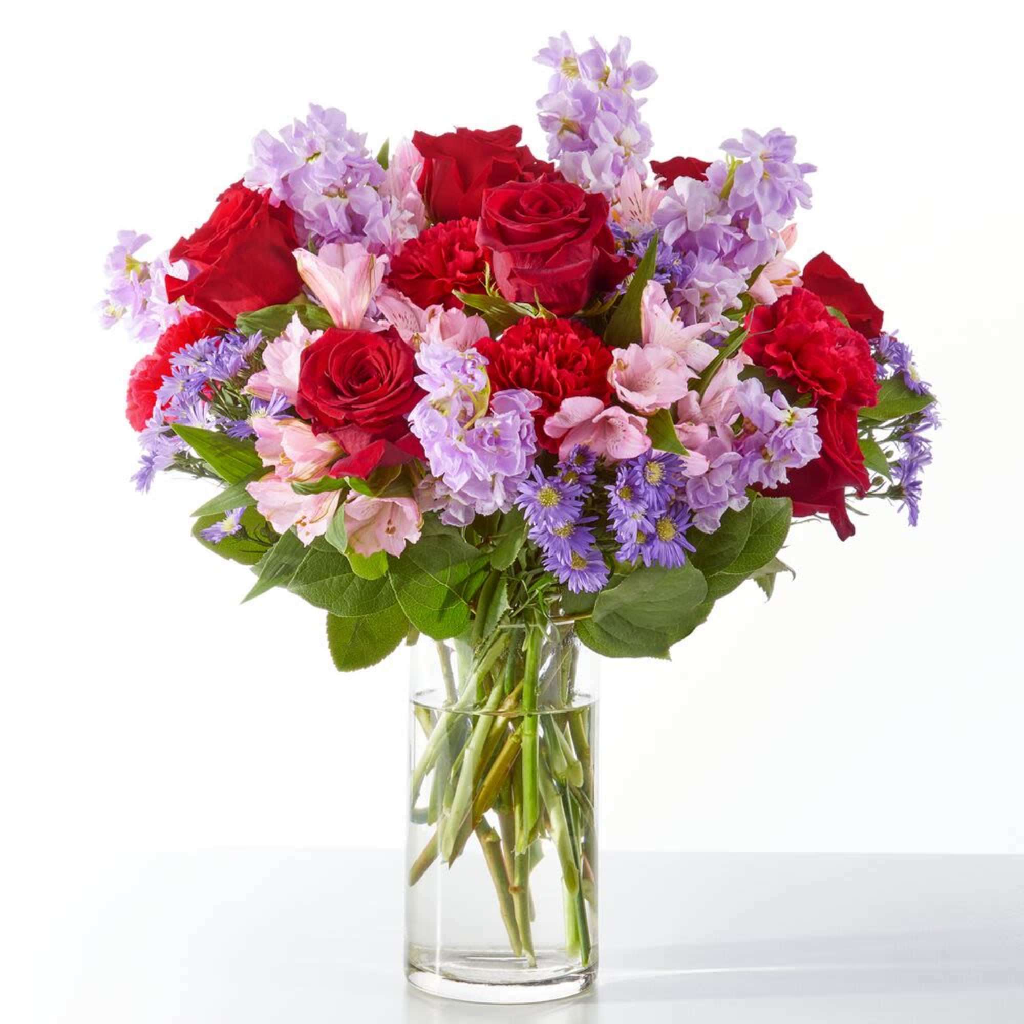 Bouquet of red roses and purple flowers in a clear glass vase