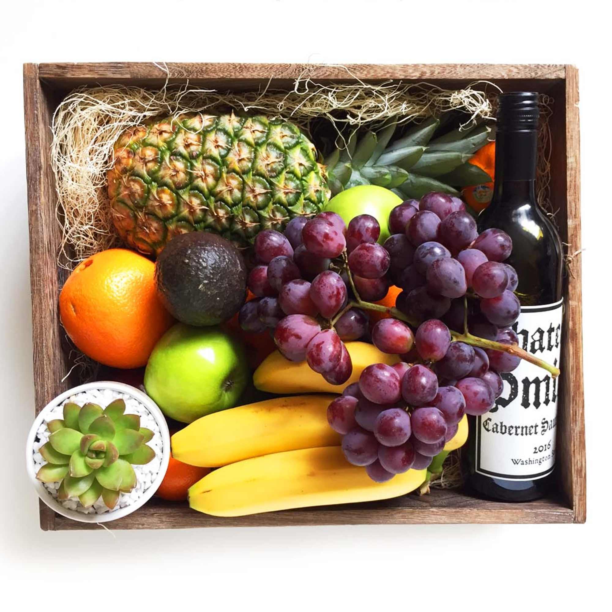 Fruit gift box with grapes, pineapple, bananas, citrus, avocado, and a wine bottle