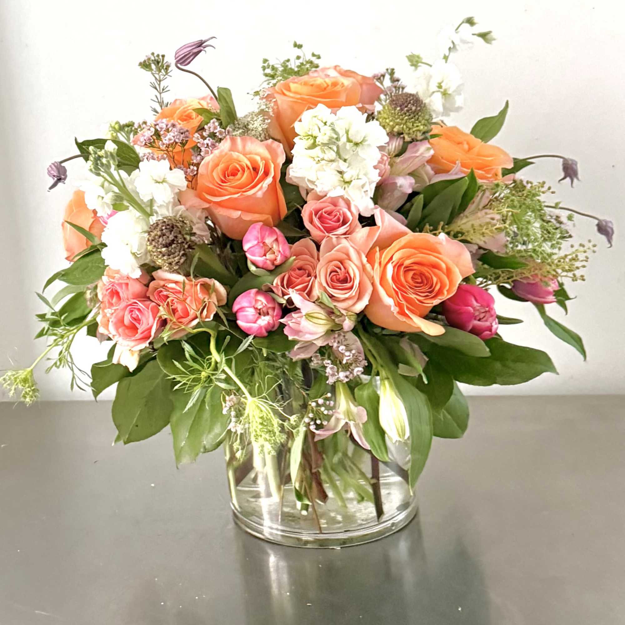 Mixed bouquet of orange and pink roses in a clear glass vase
