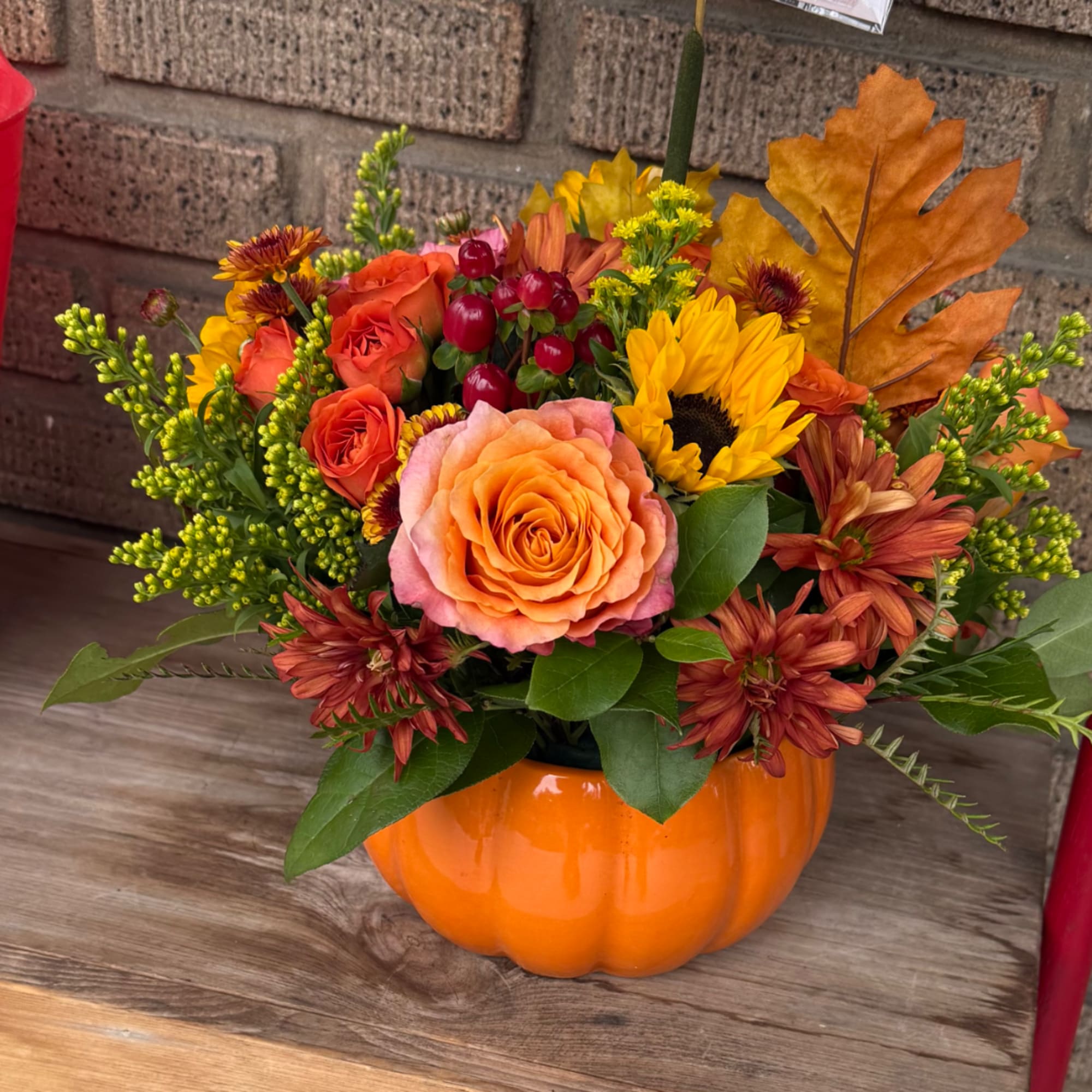 Autumn floral arrangement in an orange pumpkin vase with roses and sunflowers